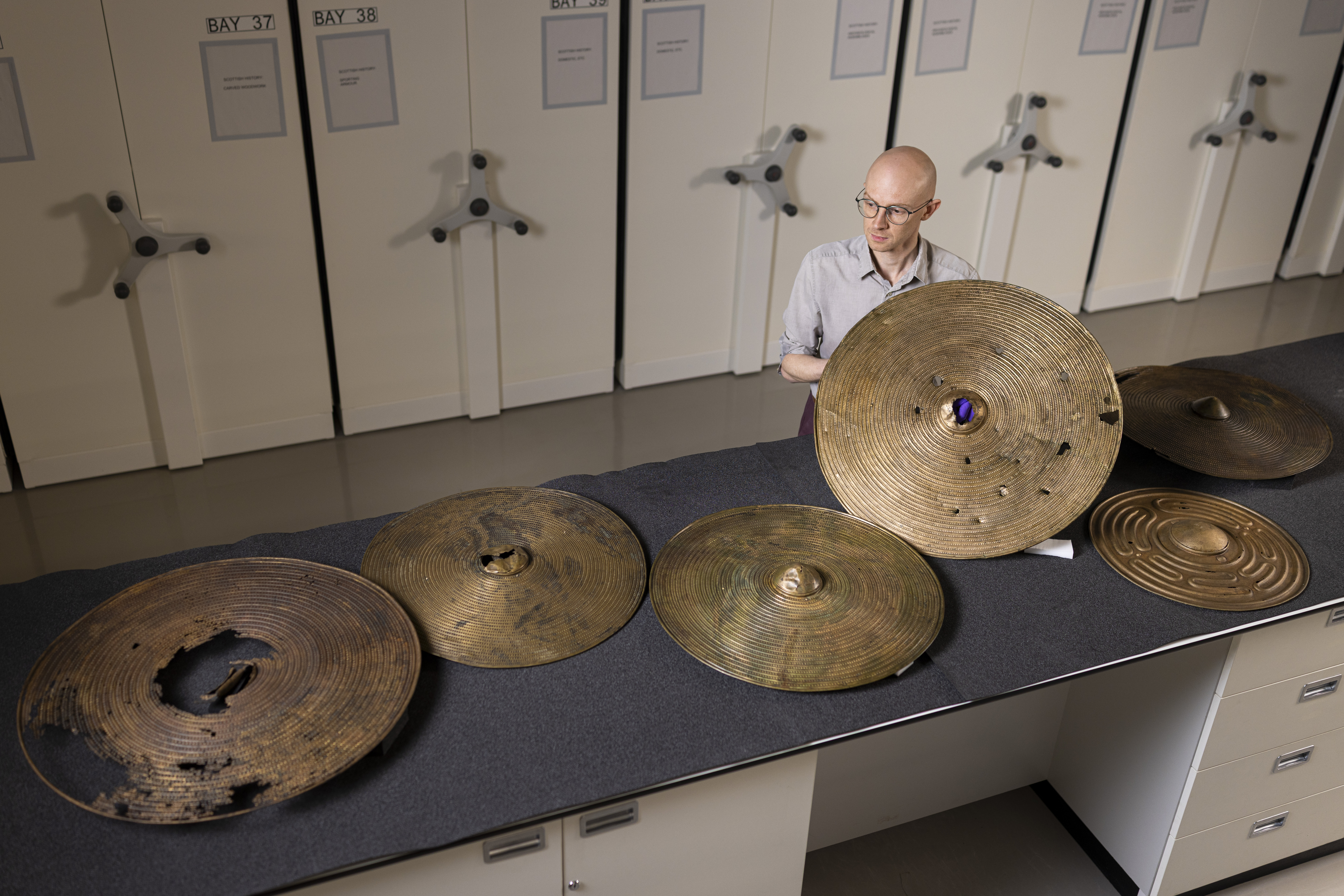 Matthew Knight holds up one Bronze Age shields, with five others lying on the bench in front of him