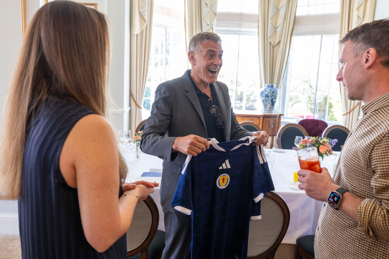 George Clooney smiles as he receives a Scotland football kit