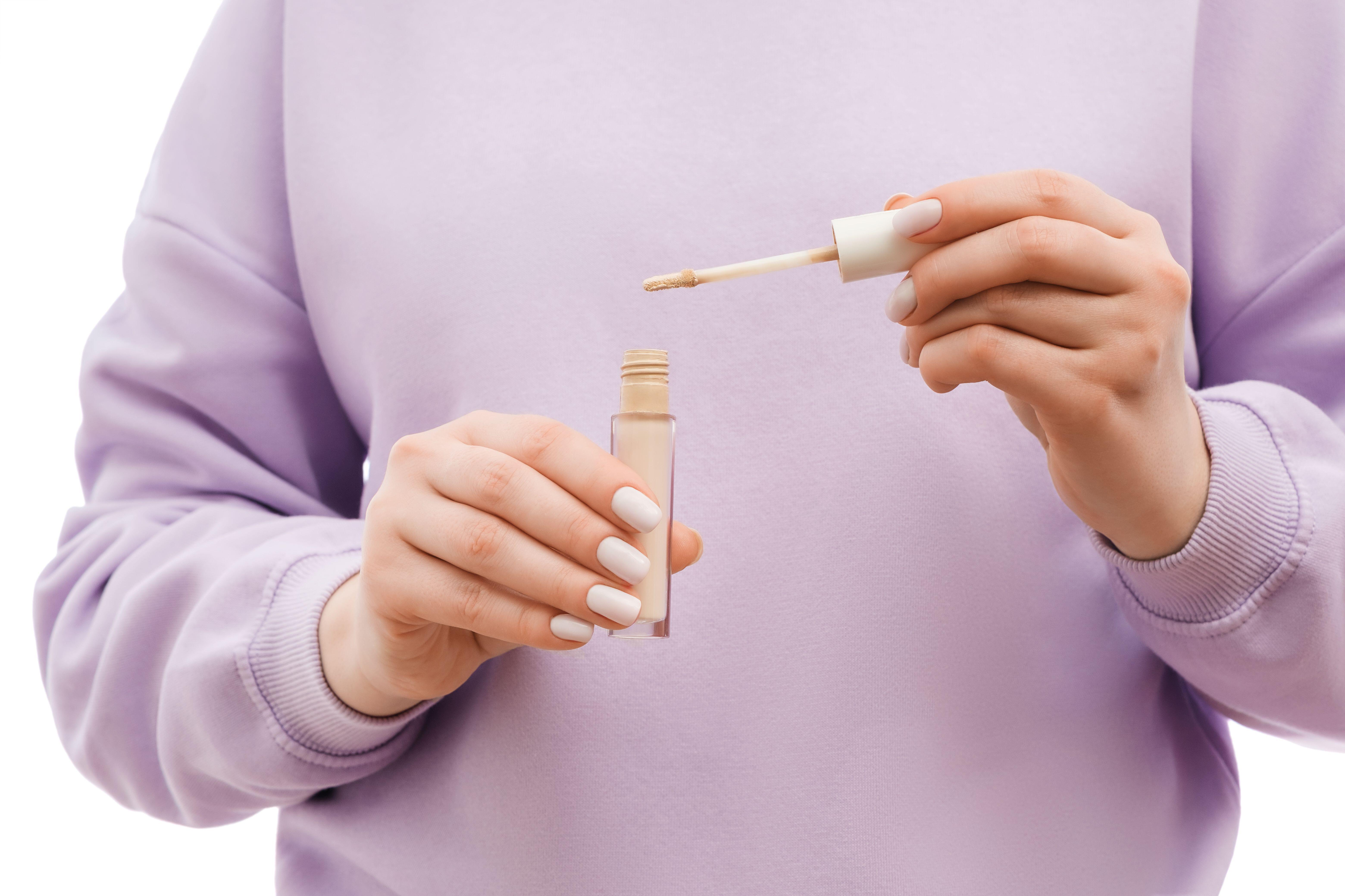 Cropped photo of woman in lavender jumper holding concealer 