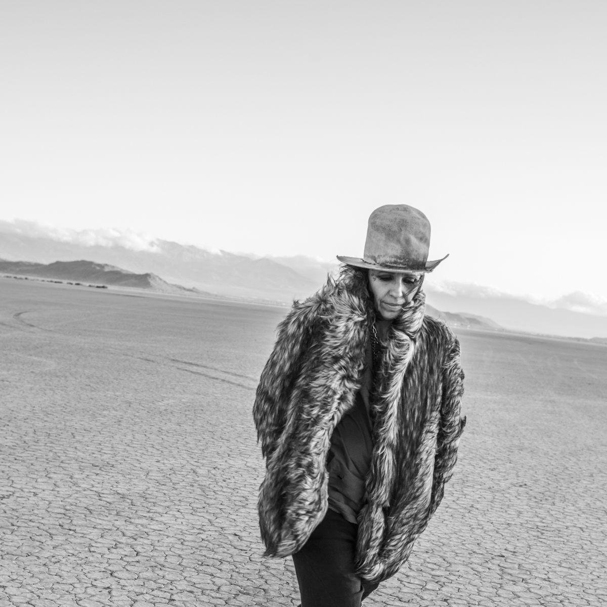 Black and white photo of Linda Perry walking on what looks like arid ground