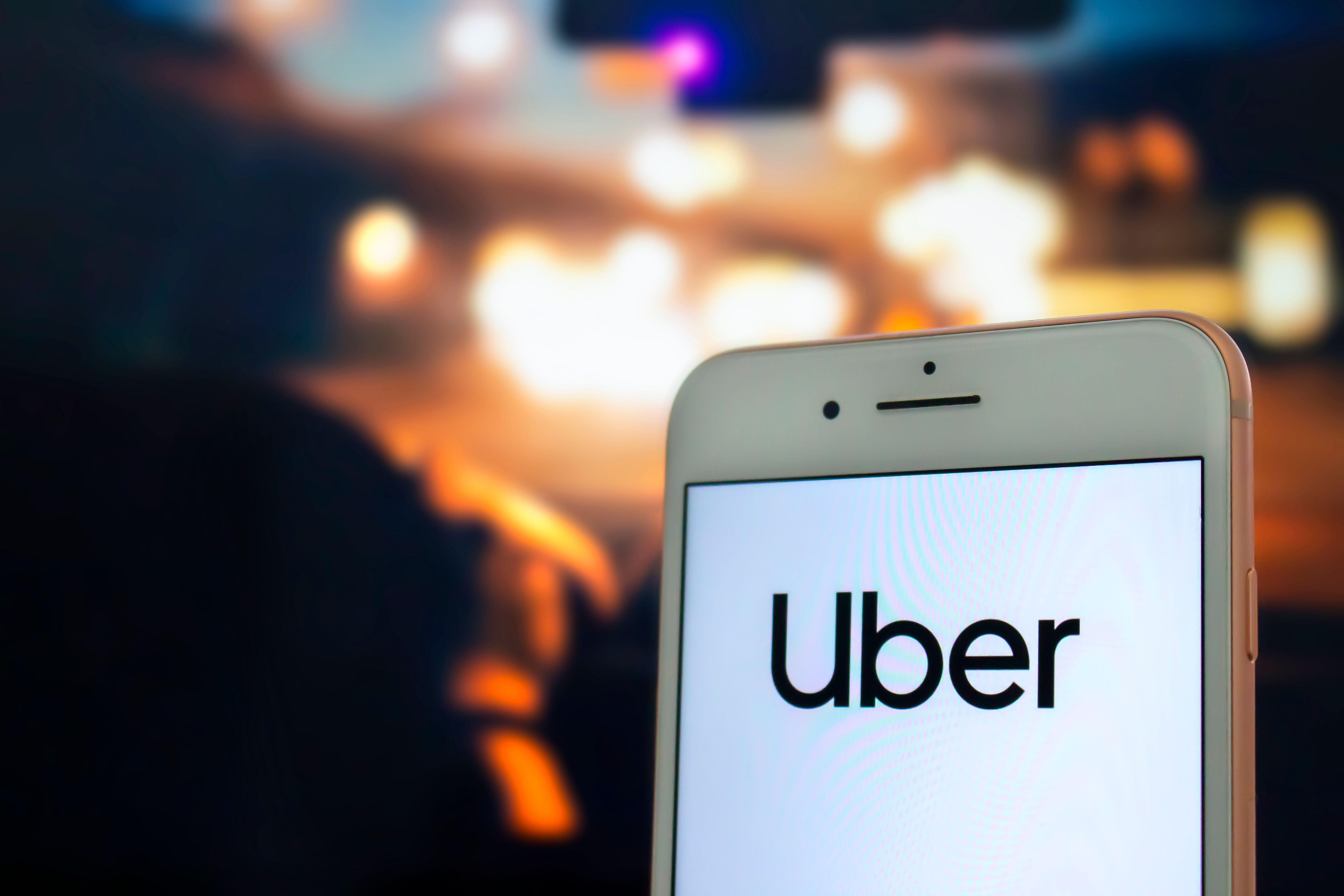 An iPhone with the Uber app open being held by a passenger in the back seat of a car