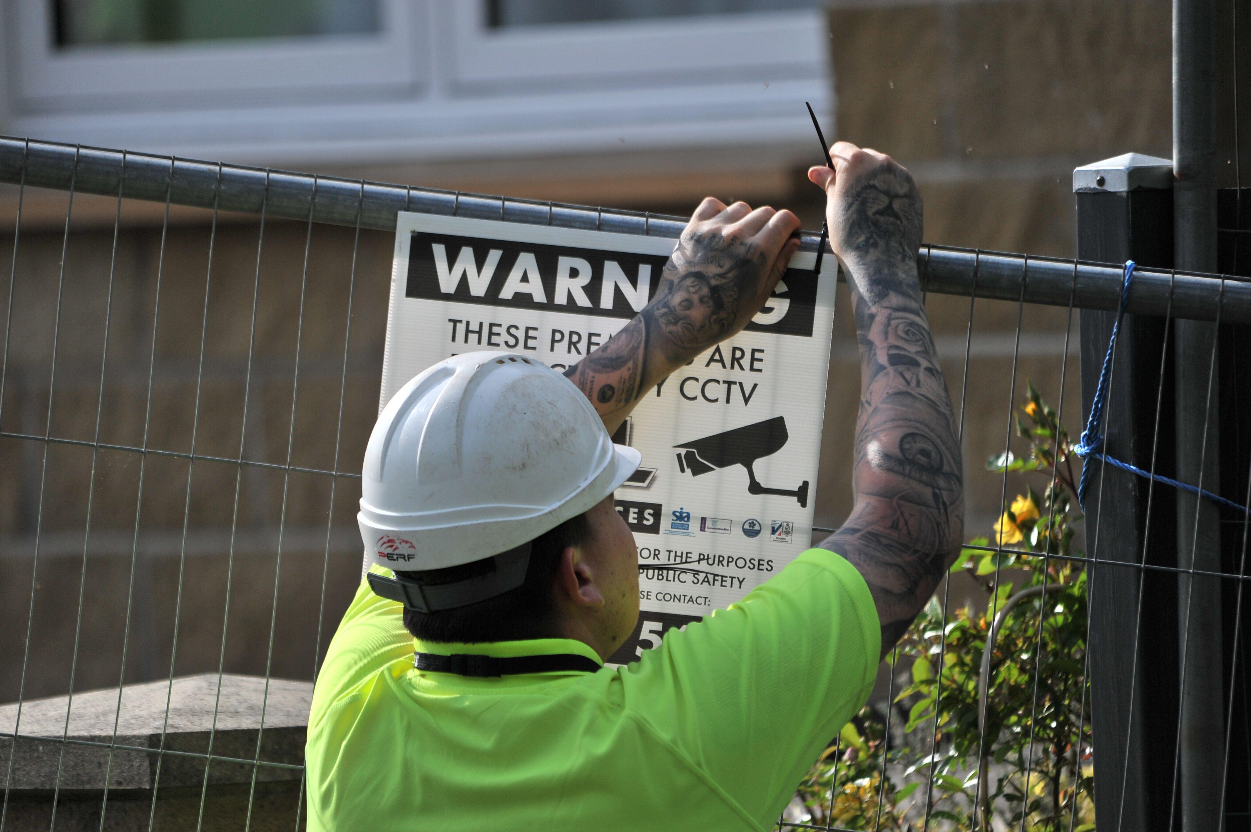 A worker in hard hat puts up a warning sign on fencing