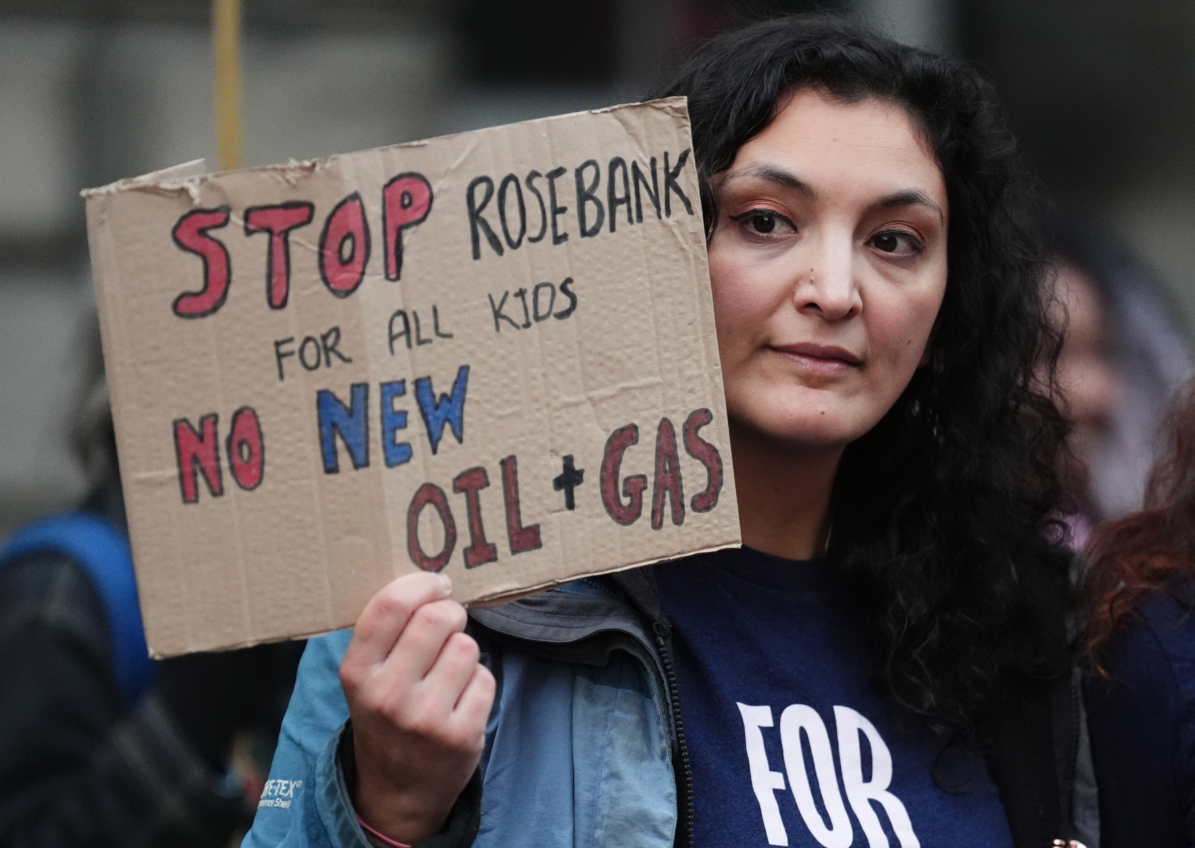 A woman holding a sign reading 'Stop Rosebank for all kids. No new oil and gas'