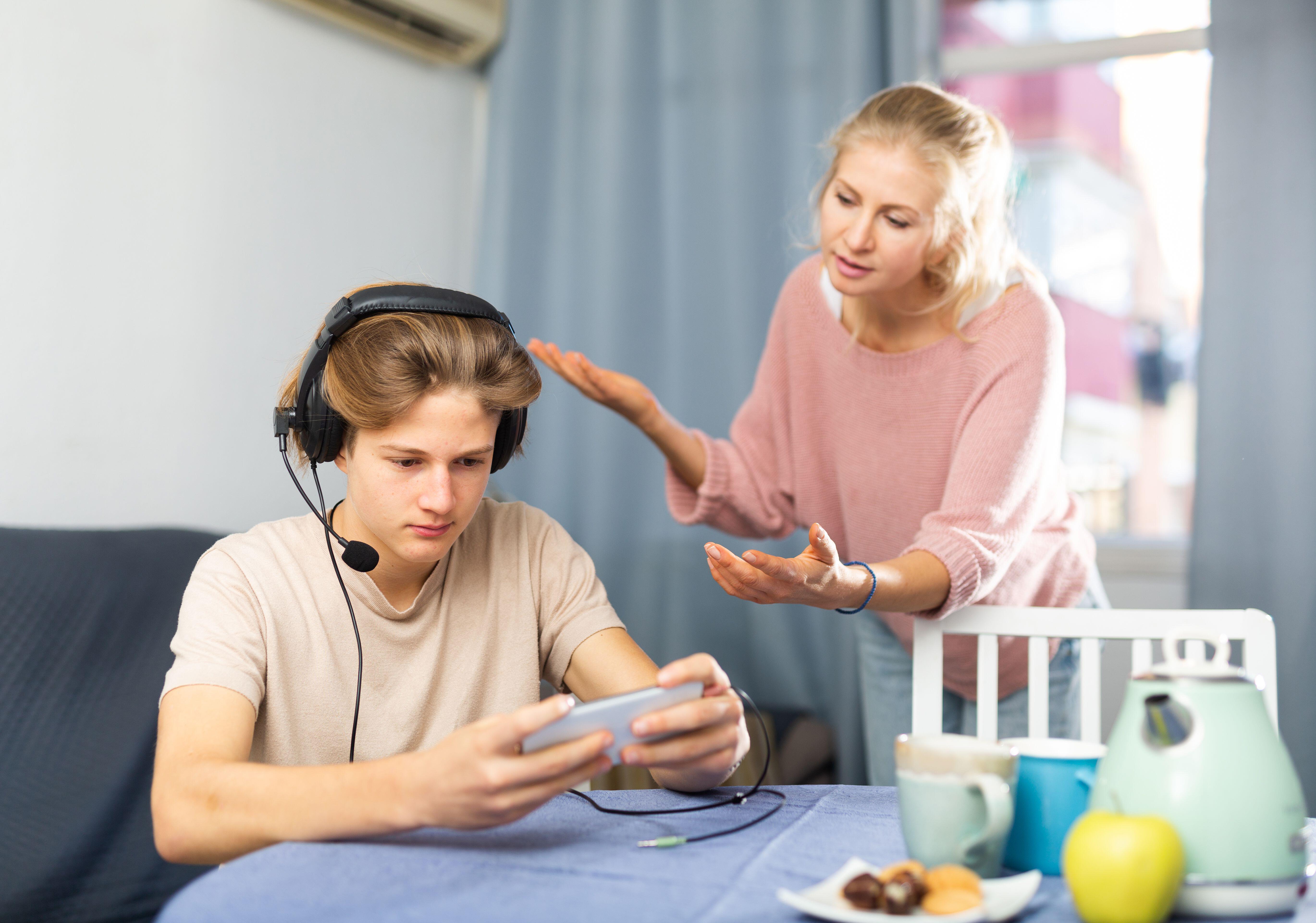 Teenager playing game on phone while upset mother talking to him