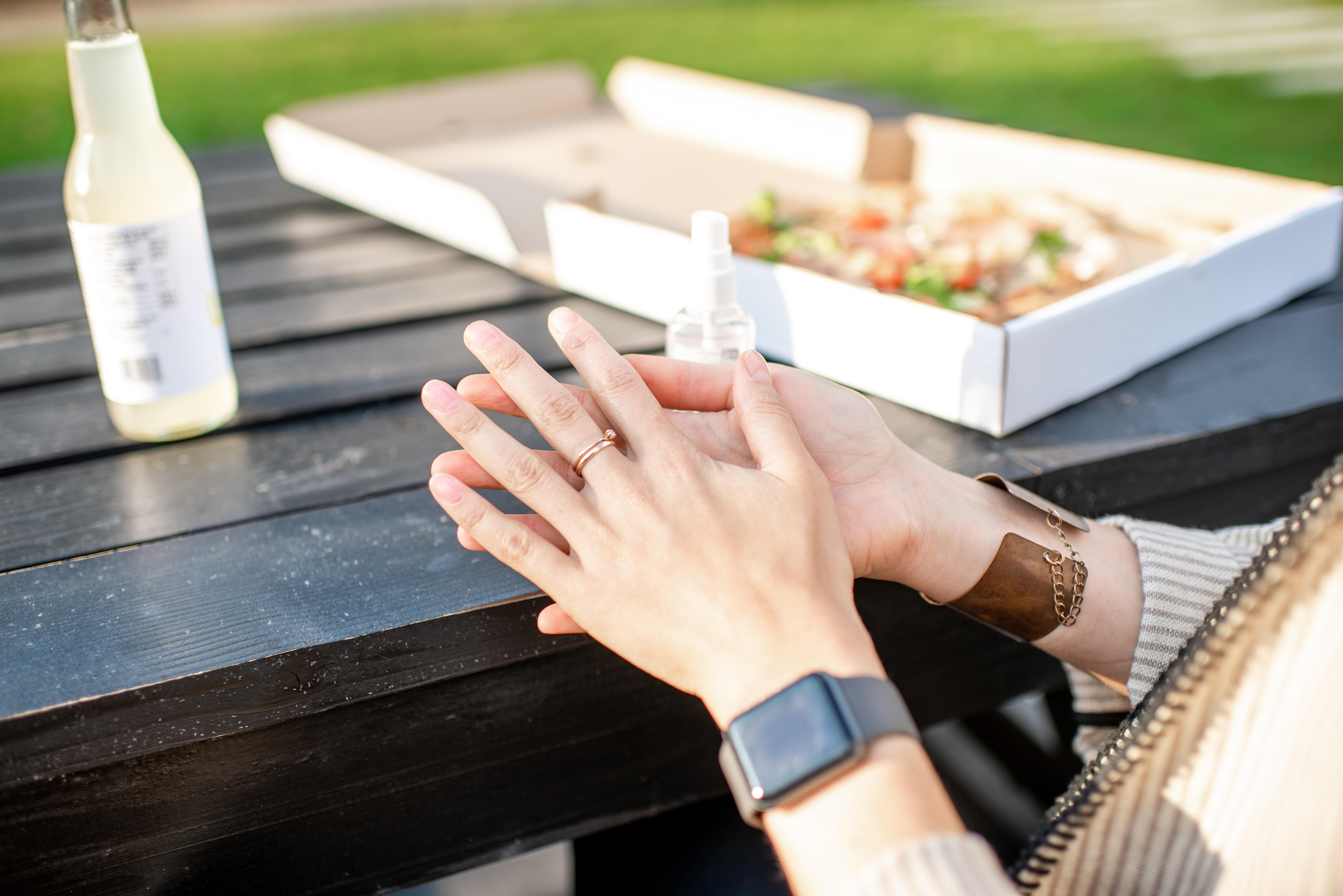 Woman sprinkling antiseptic on the hands before eating pizza outdooors