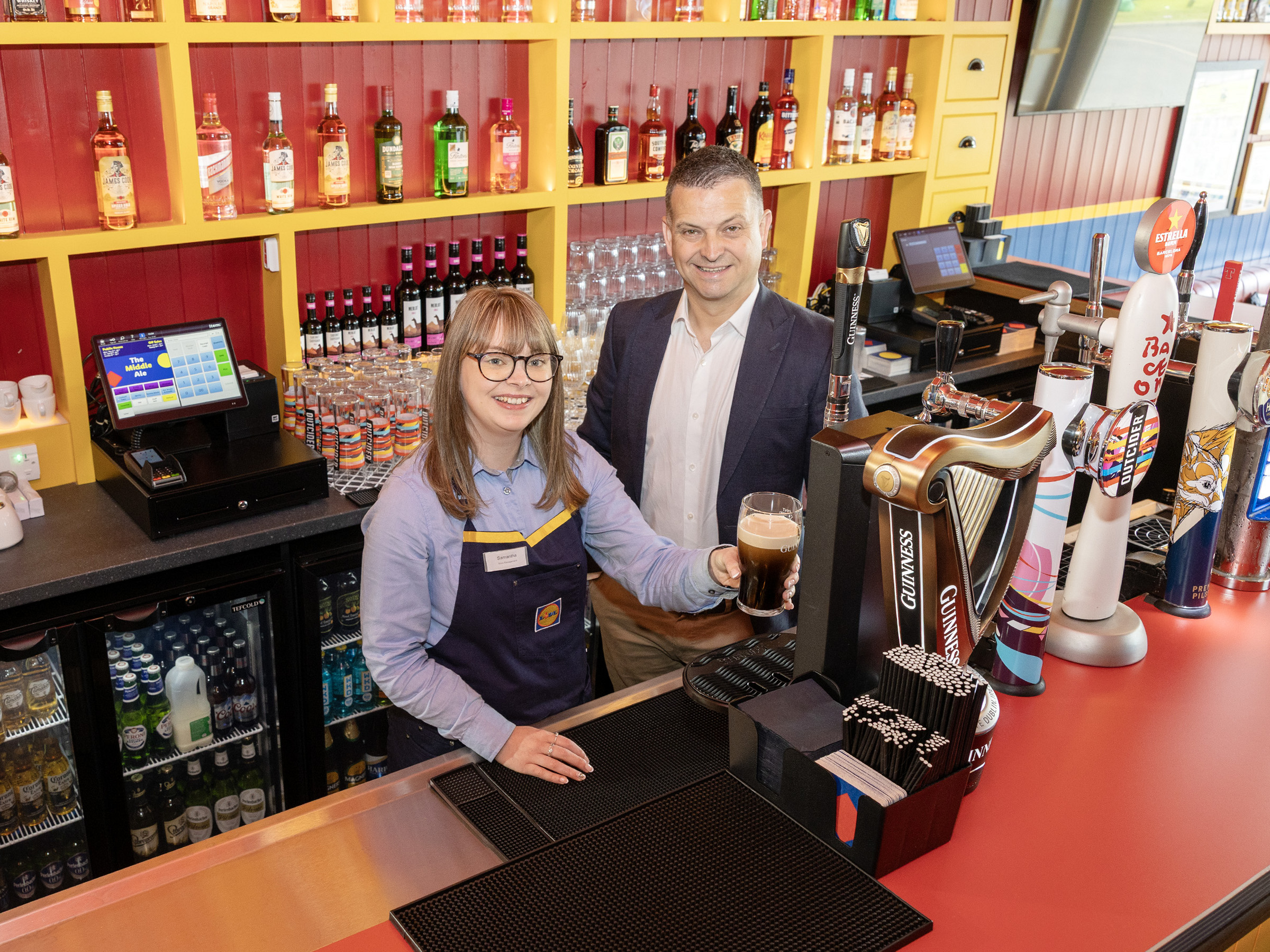 Samantha Hill smiling while pulling a pint behind the bar alongside Gordon Cruikshanks