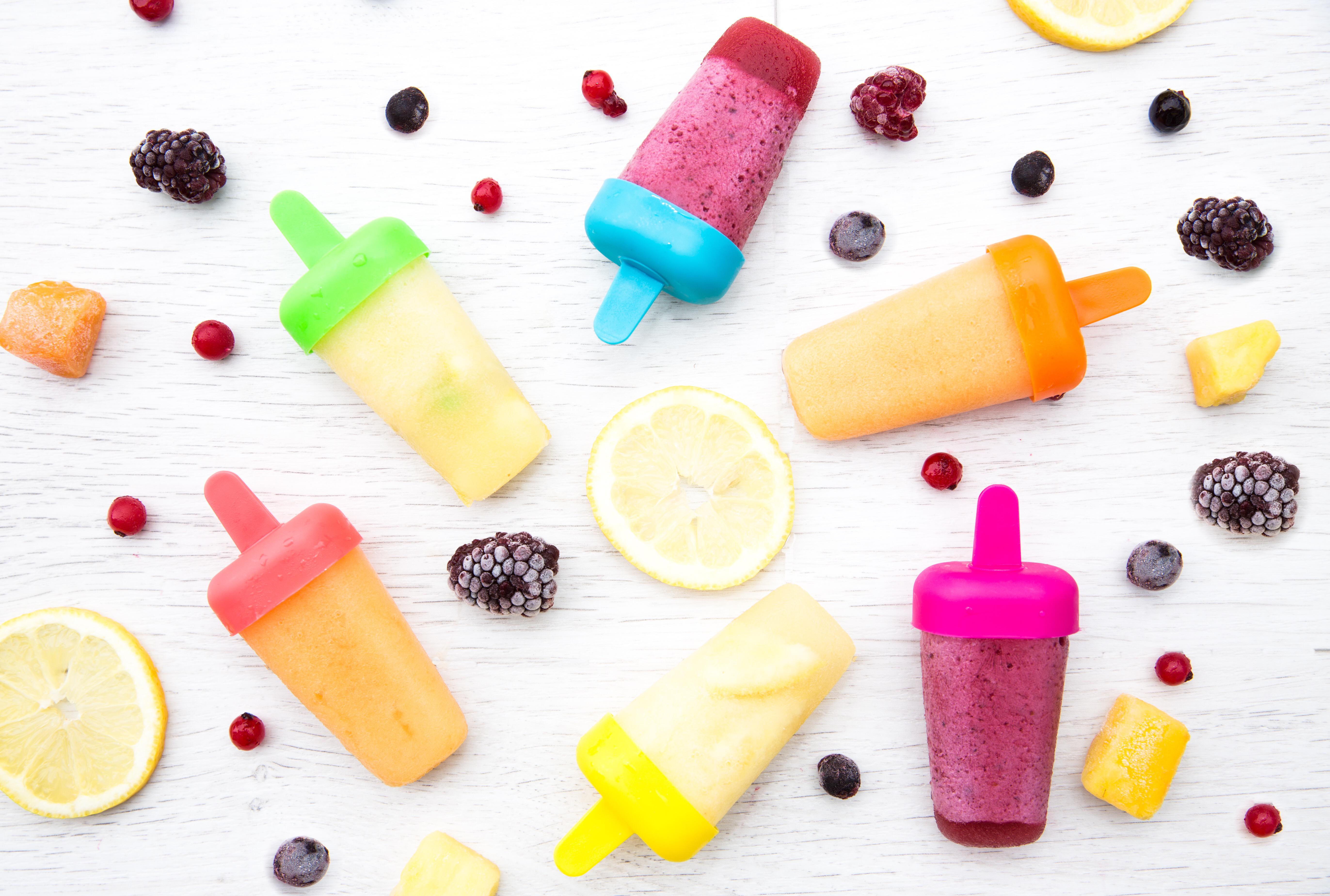 Colourful ice lollies laid out on a table next to frozen fruit