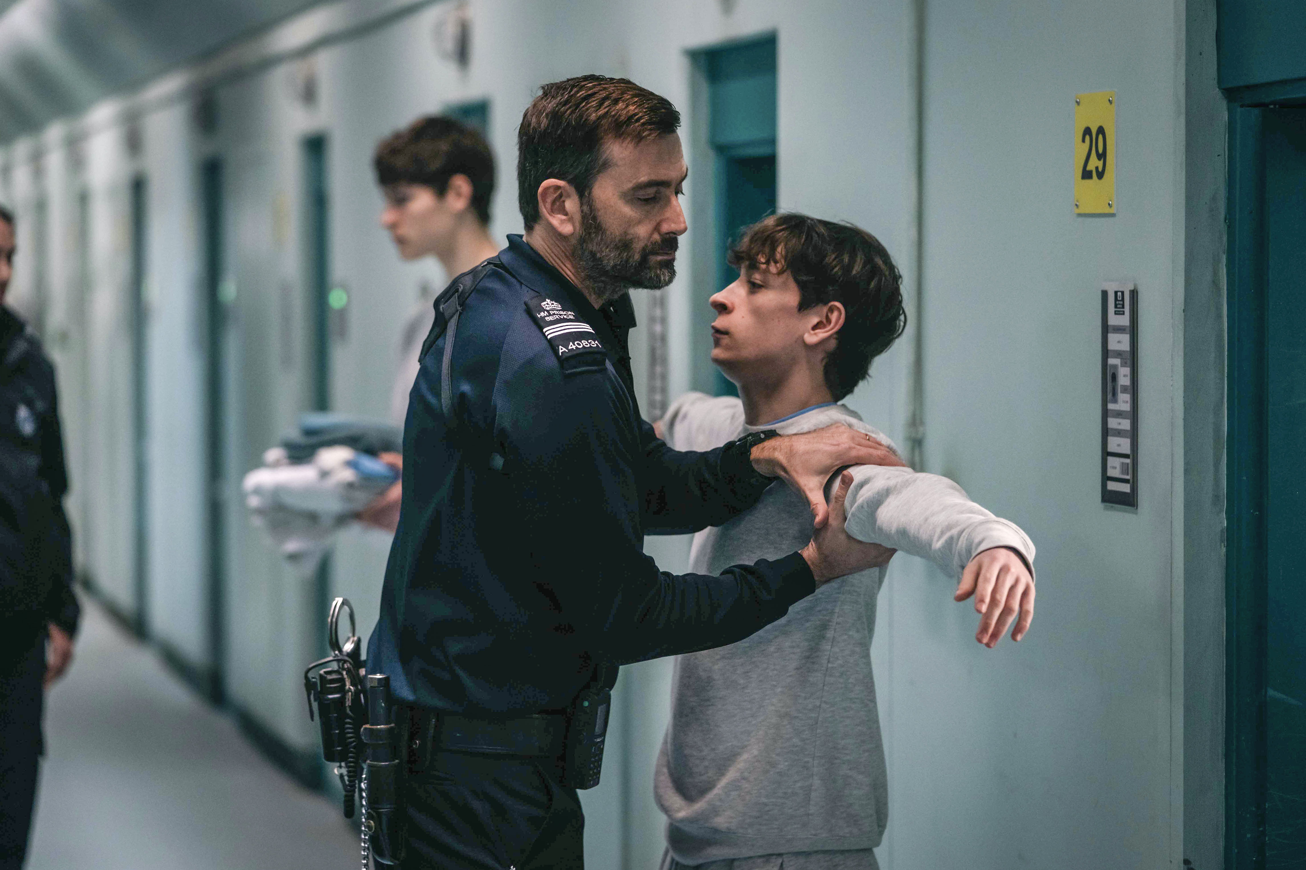 David Tennant in character as a prison officer searching a teenage criminal in a prison