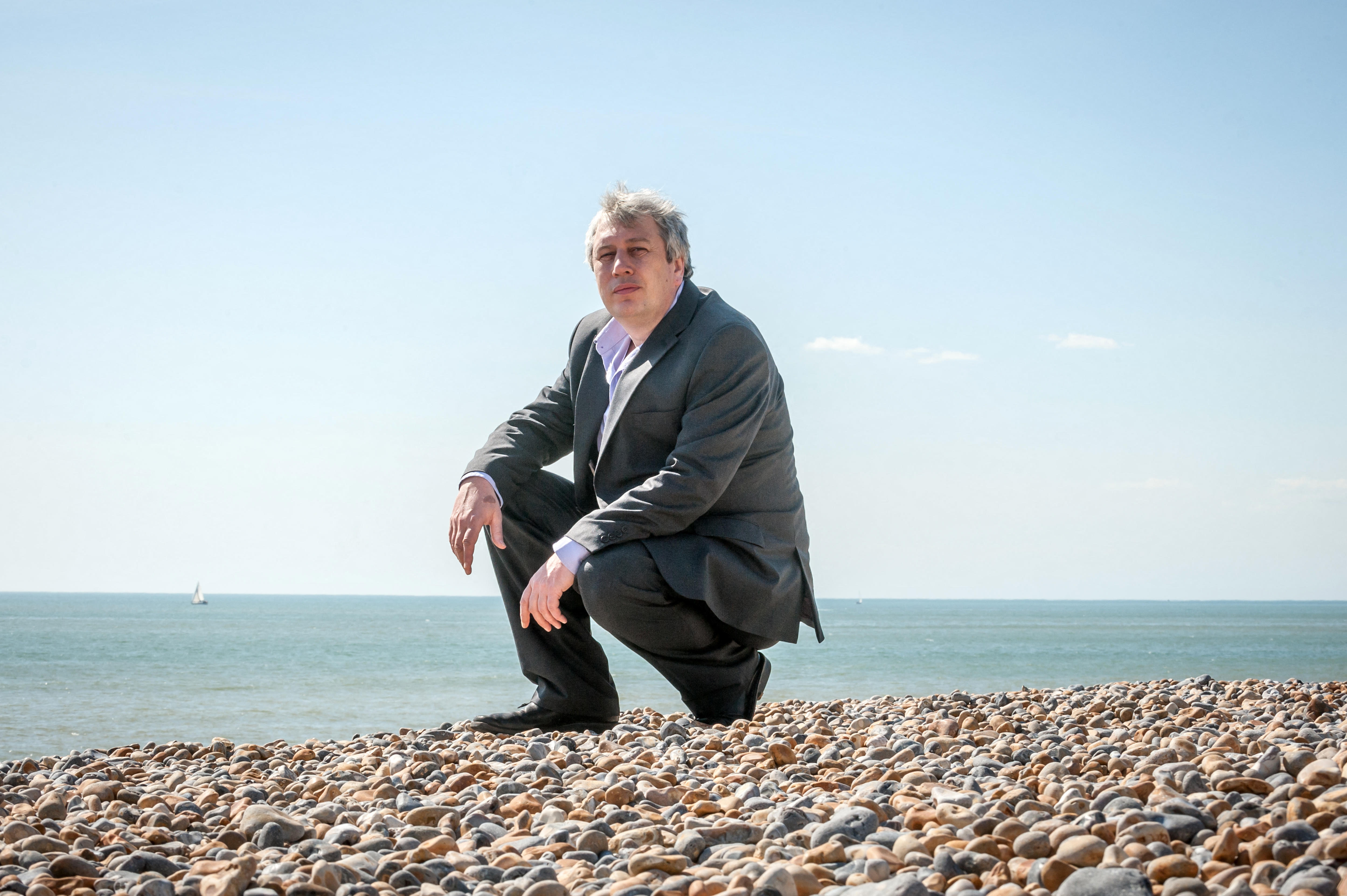 Rod Liddle squatting on a beach