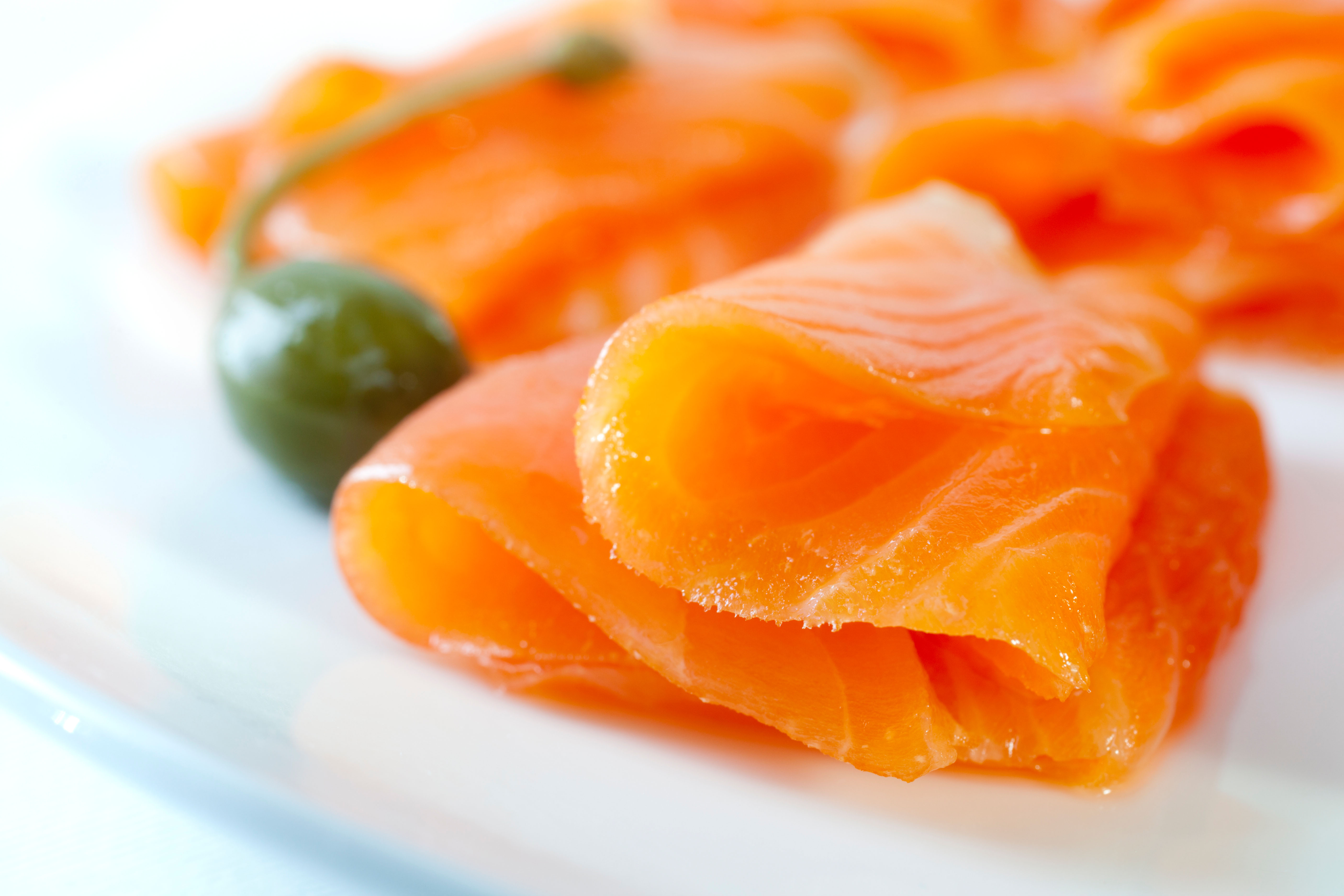 Cold smoked salmon on a white plate with a caperberry