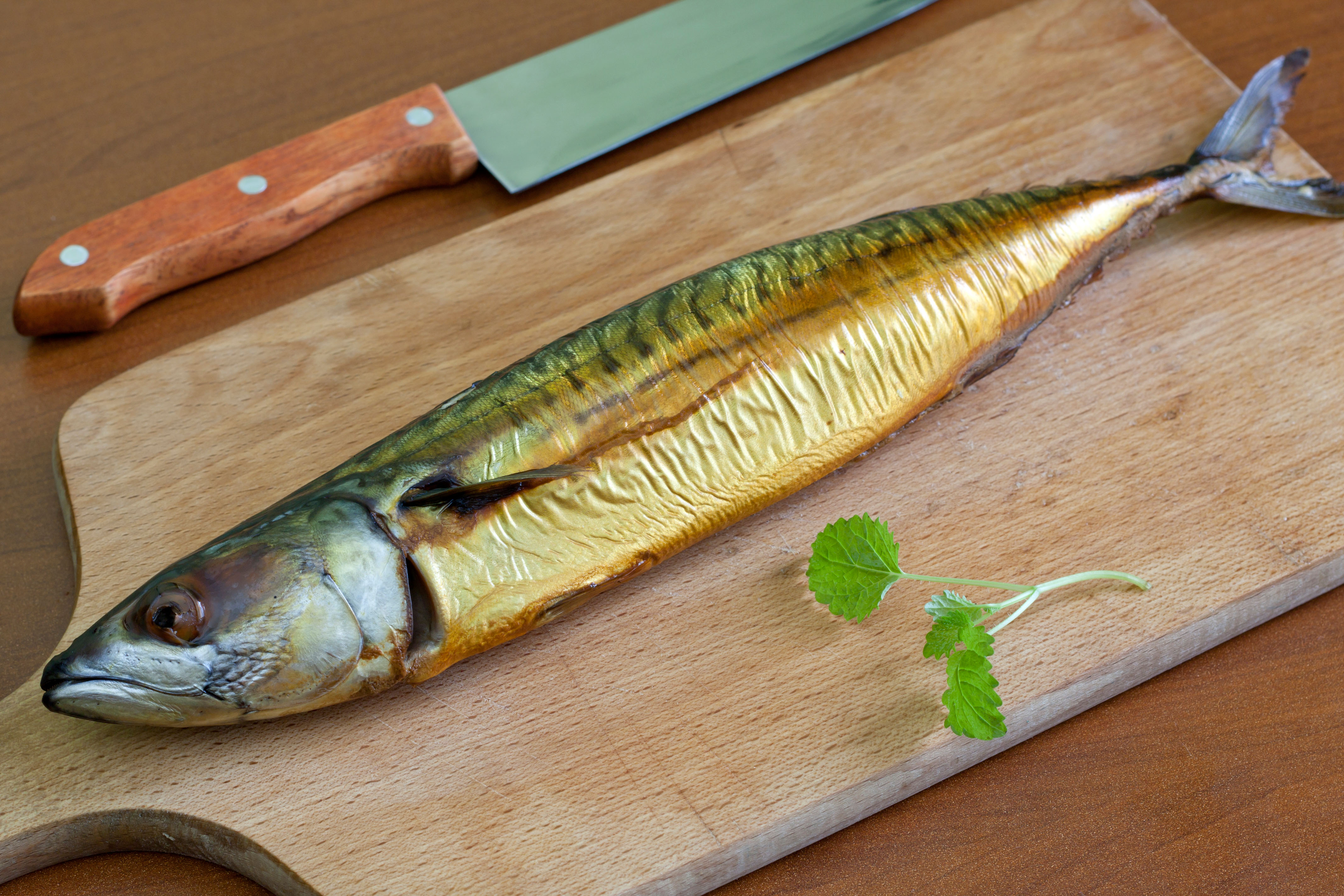 Smoked mackerel on a wooden chopping board next to a knife 