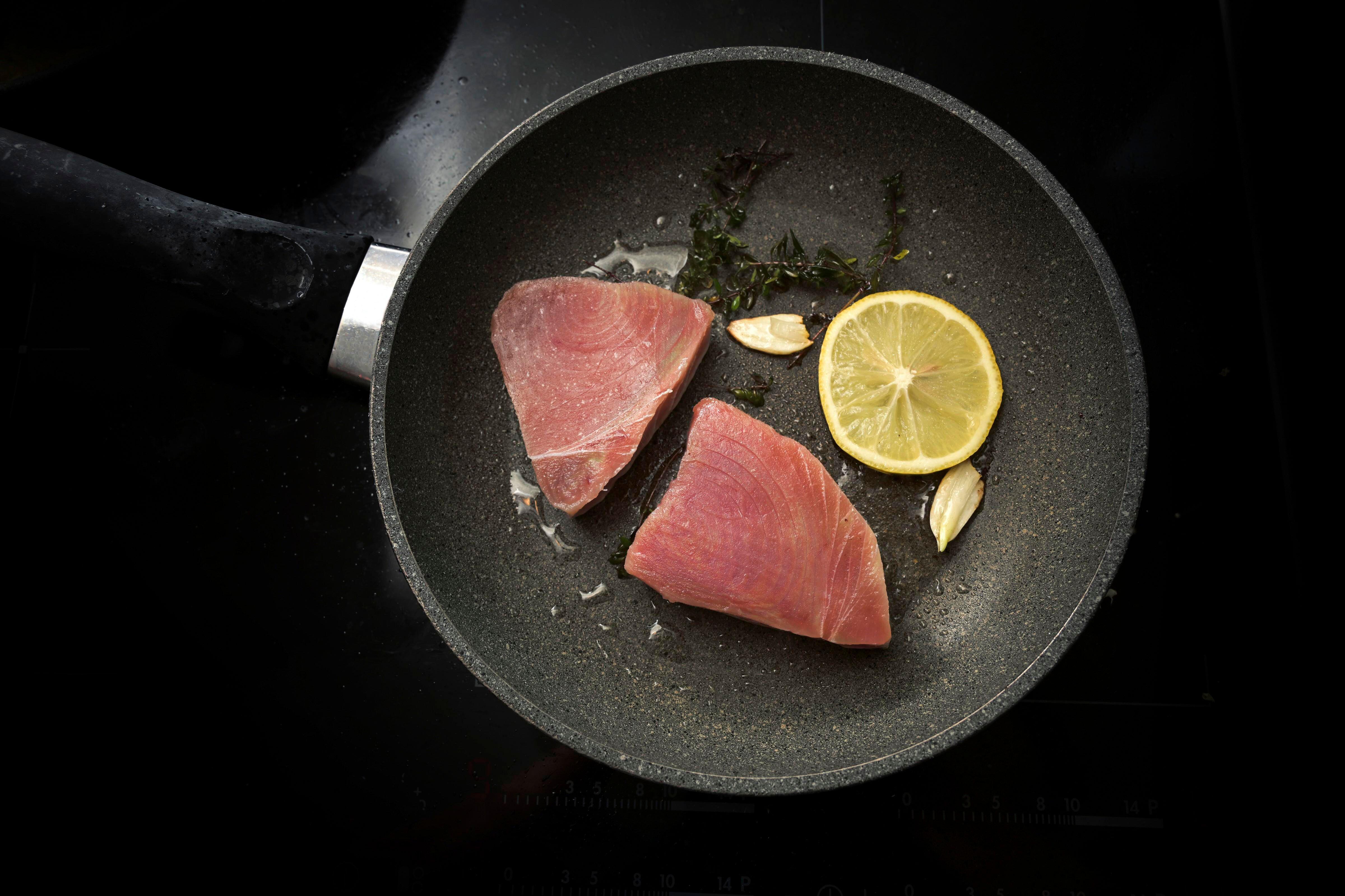  Fresh raw tuna steaks with lemon, garlic and thyme herb in a frying pan
