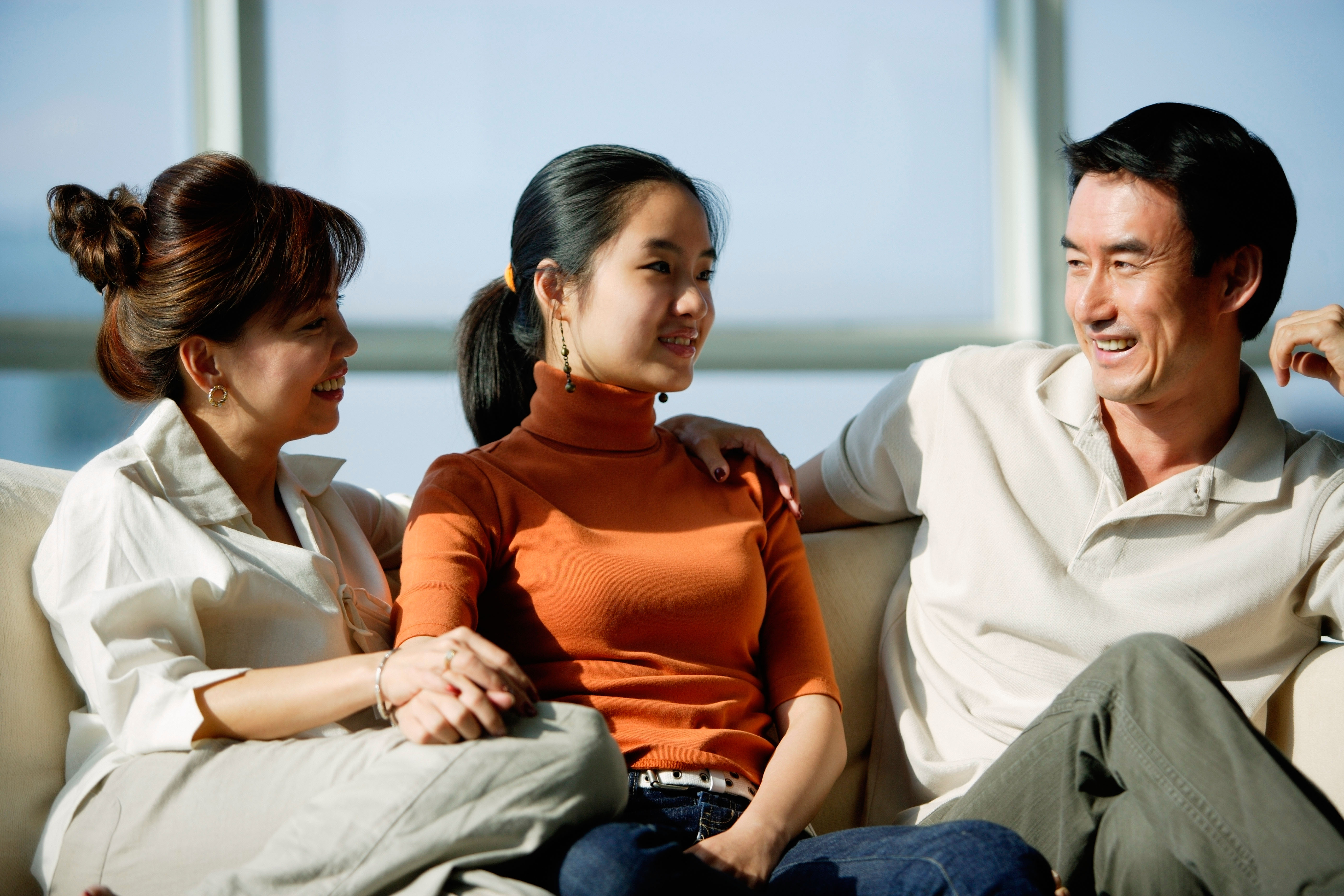 Parents having a conversation with teenage girl about money on sofa