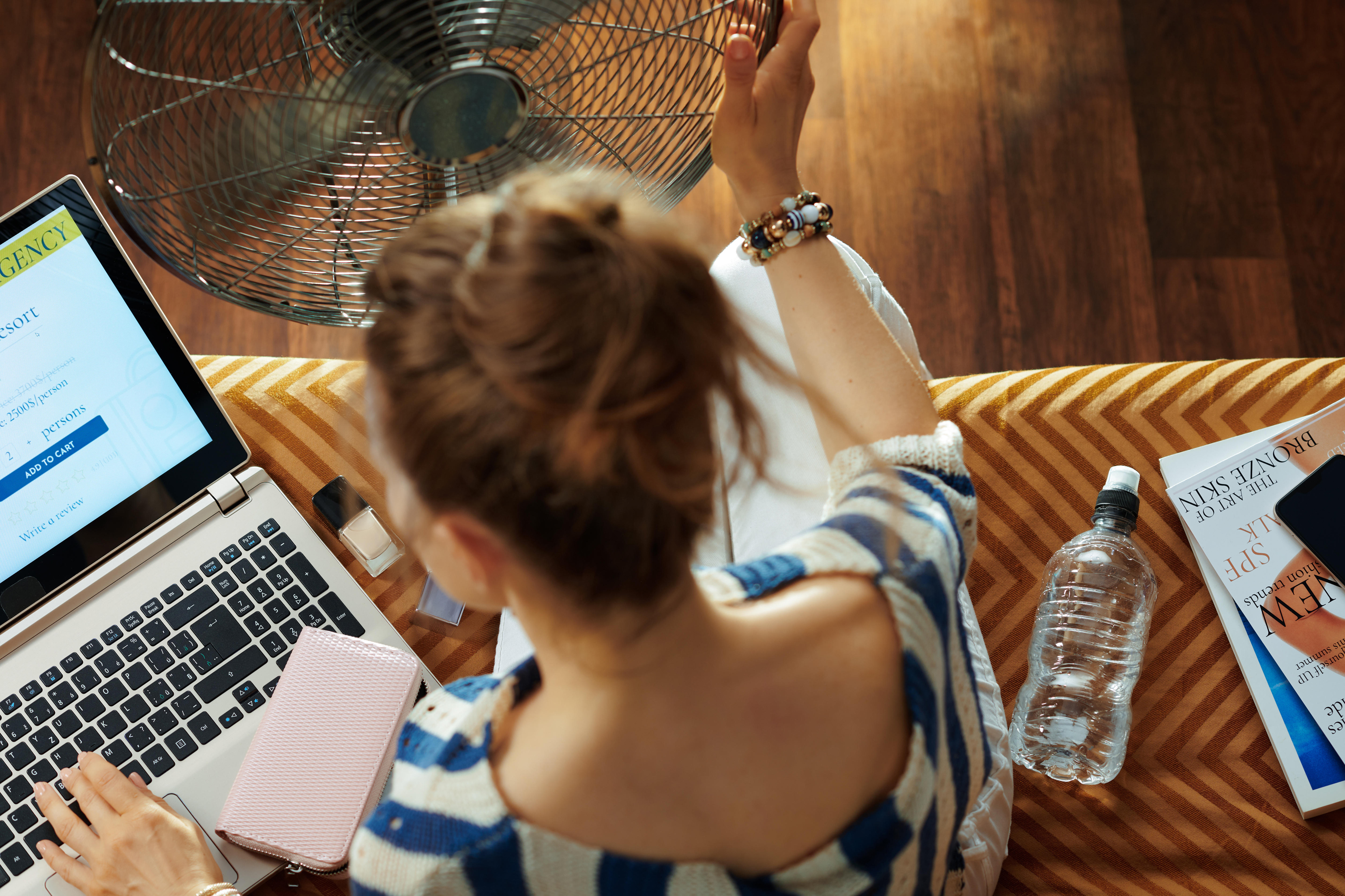 Woman at home using a fan to stay cool while working on her laptop