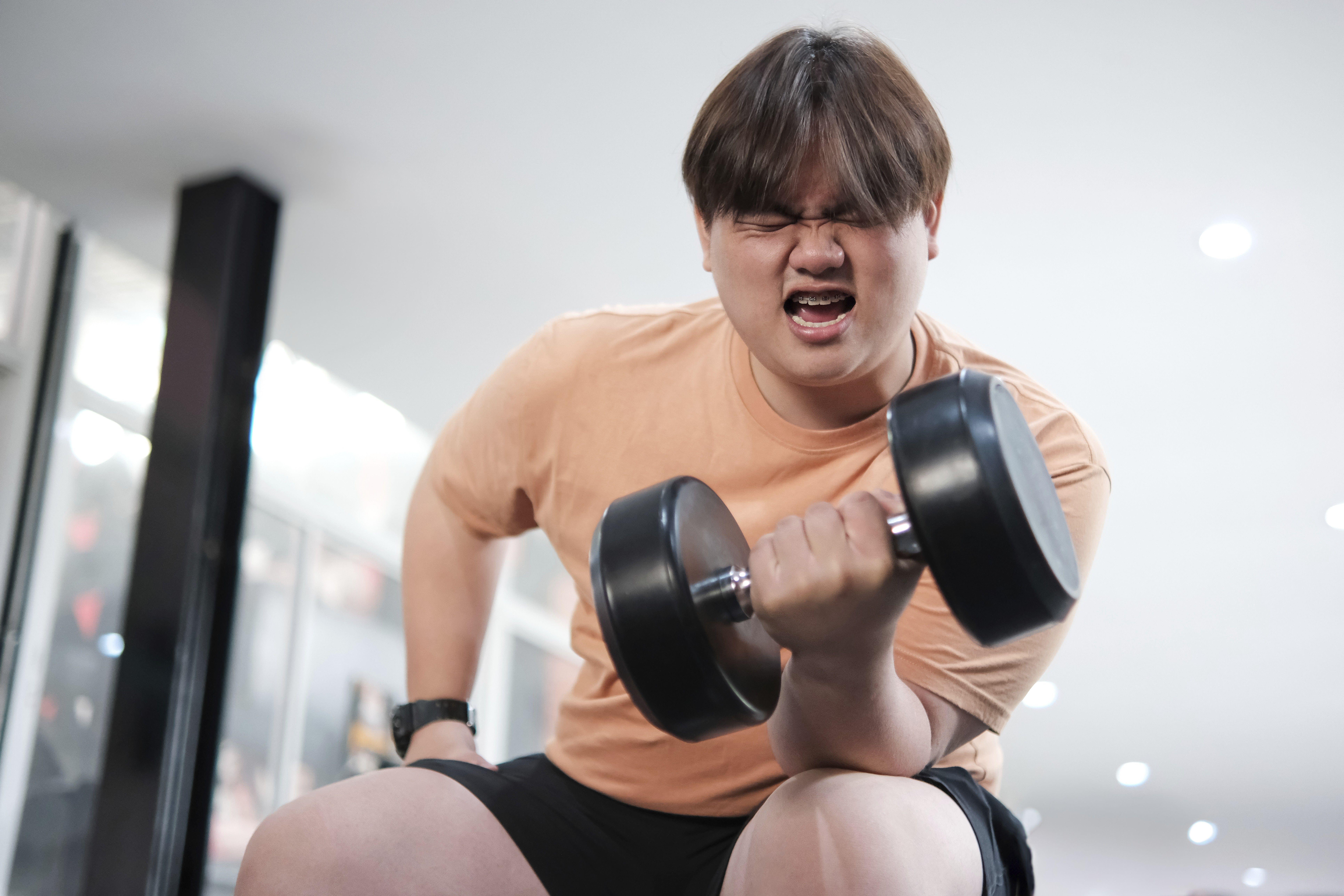 A young man in an orange Tshirt lifting weights looking angry