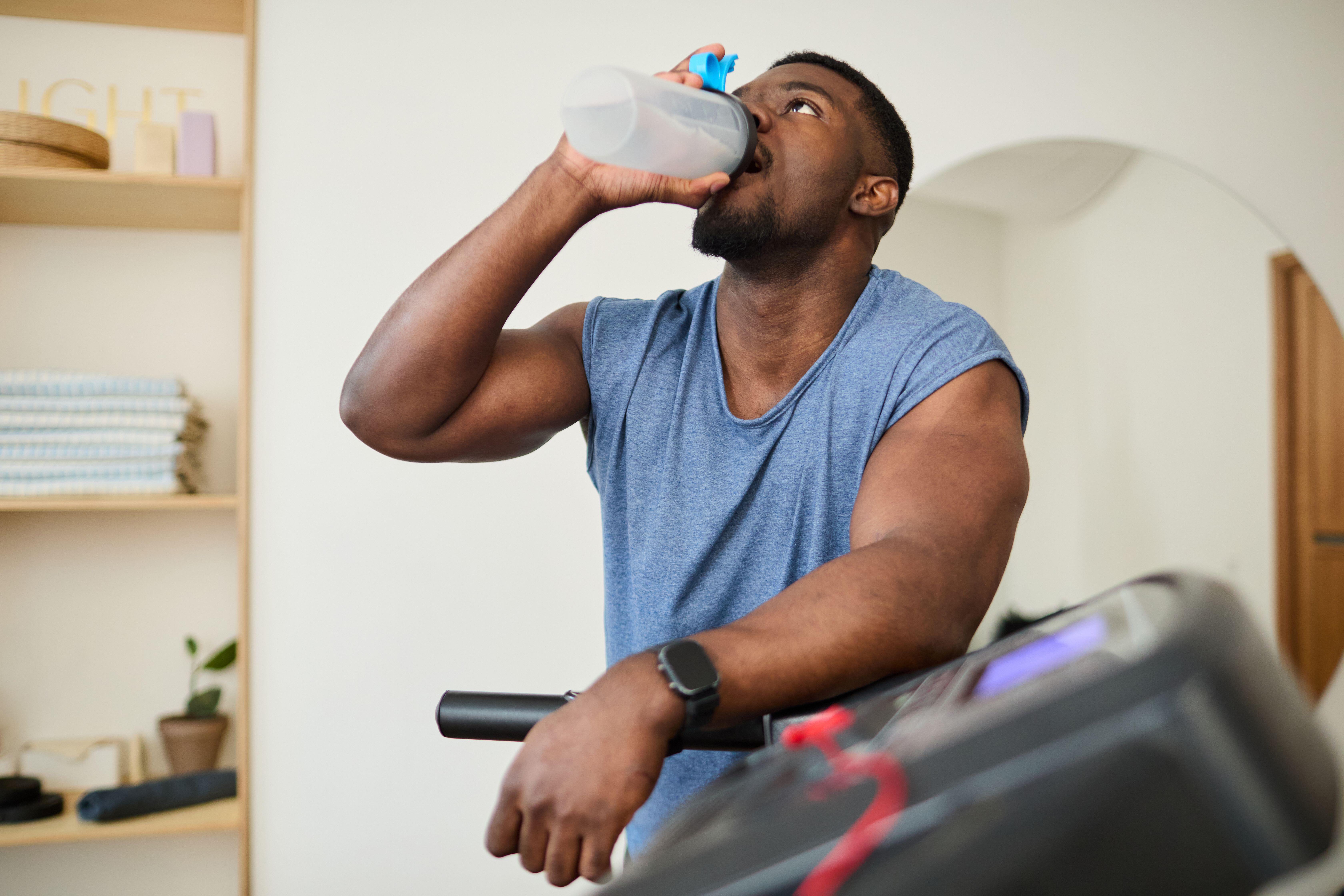 Man leaning on treadmill and drinking water during workout