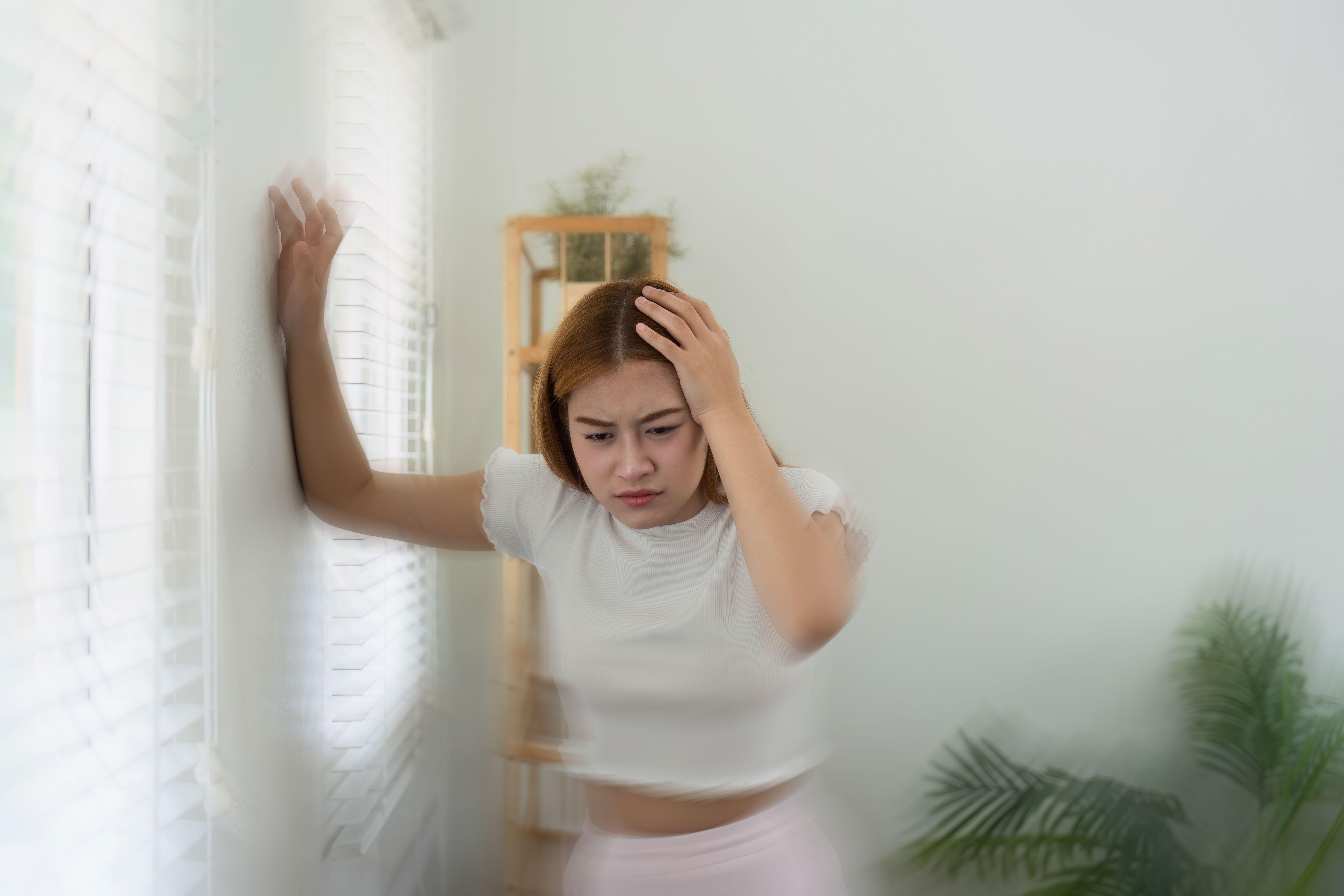 Dizzy young woman leaning on a wall at home