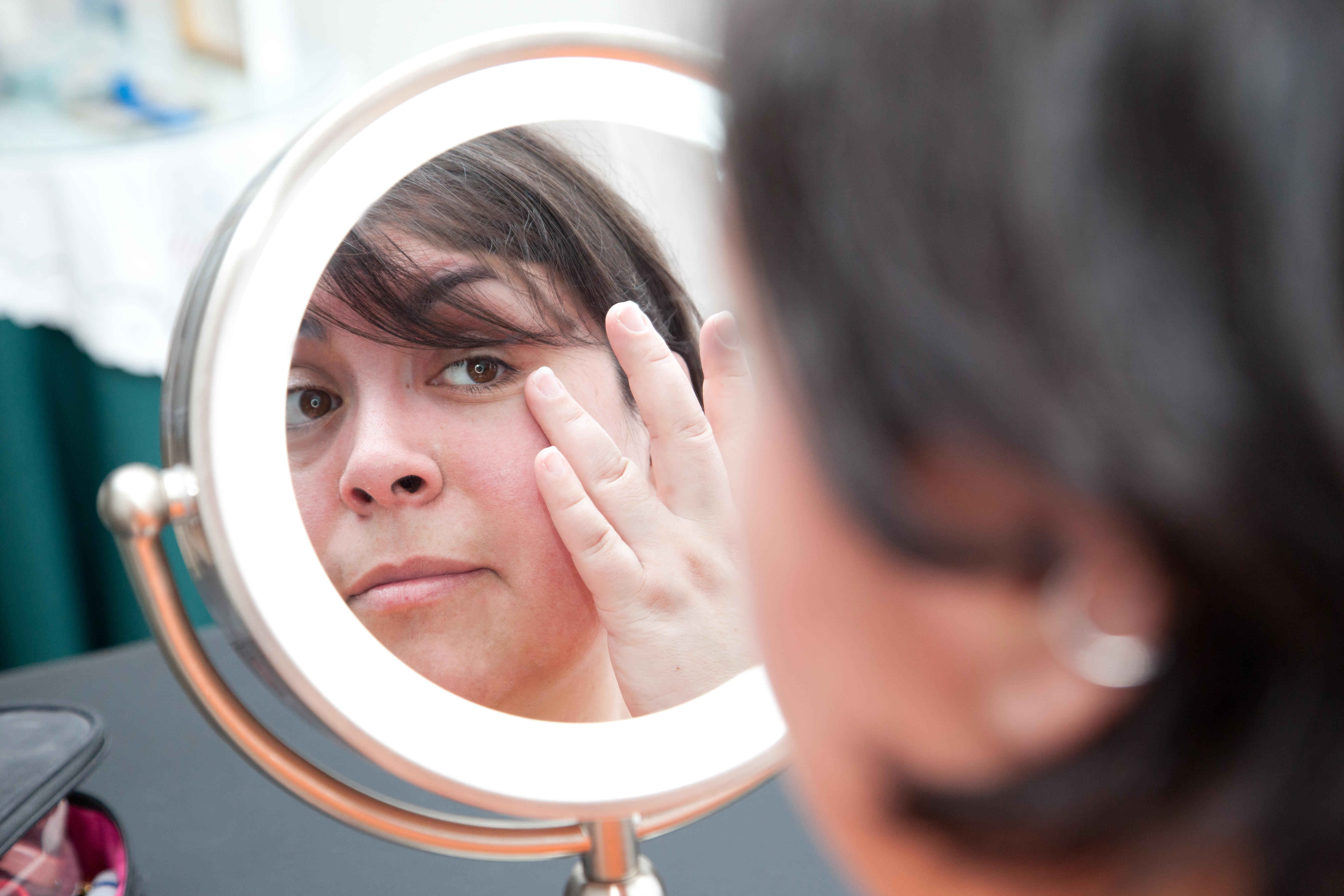  A woman looks at herself in a mirror and looks at her pores and skin, touching her eye
