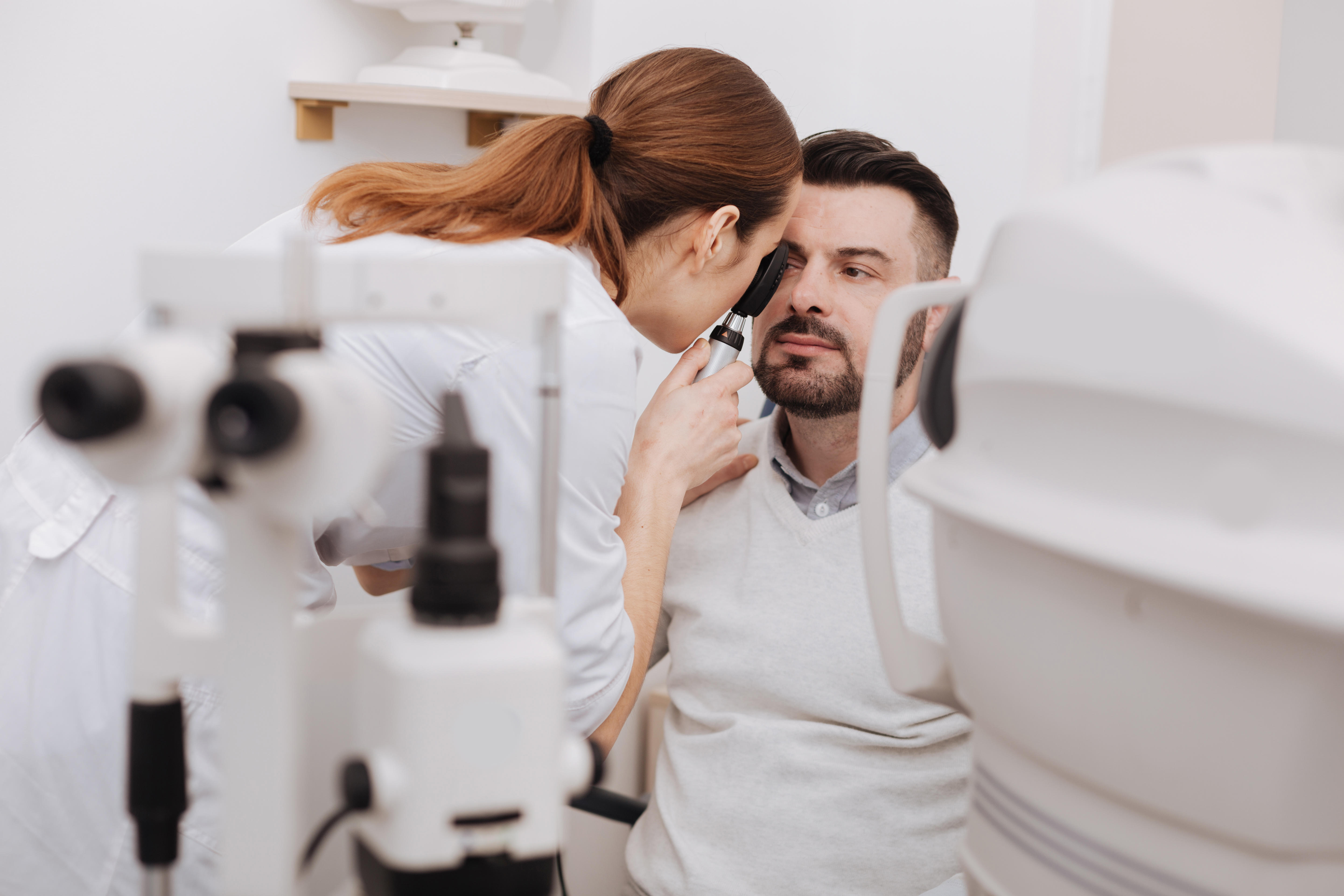 Professional experienced optometrist using an ophthalmoscope to look at patient's eyes 