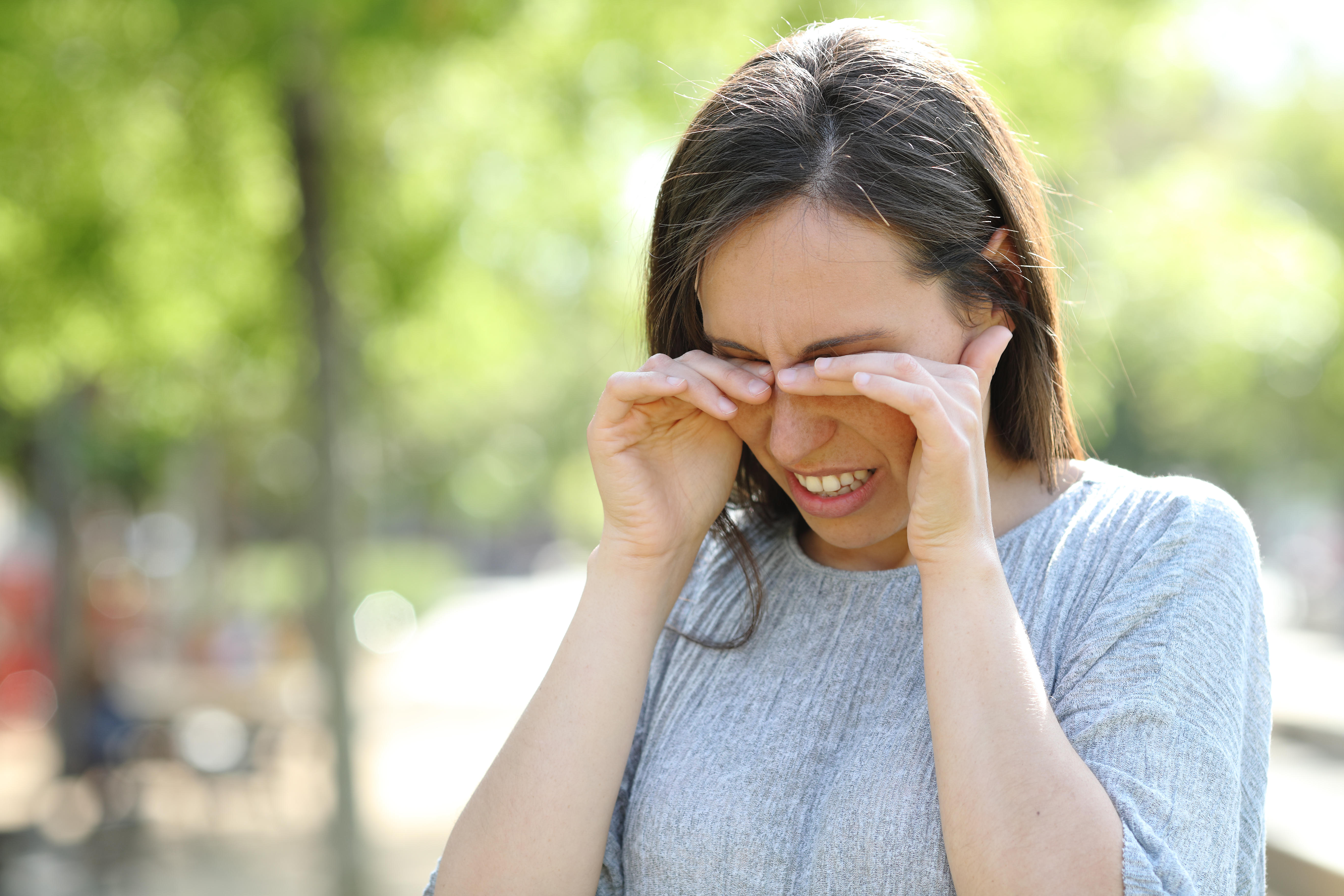 Woman rubbing her eyes standing outdoors in a park