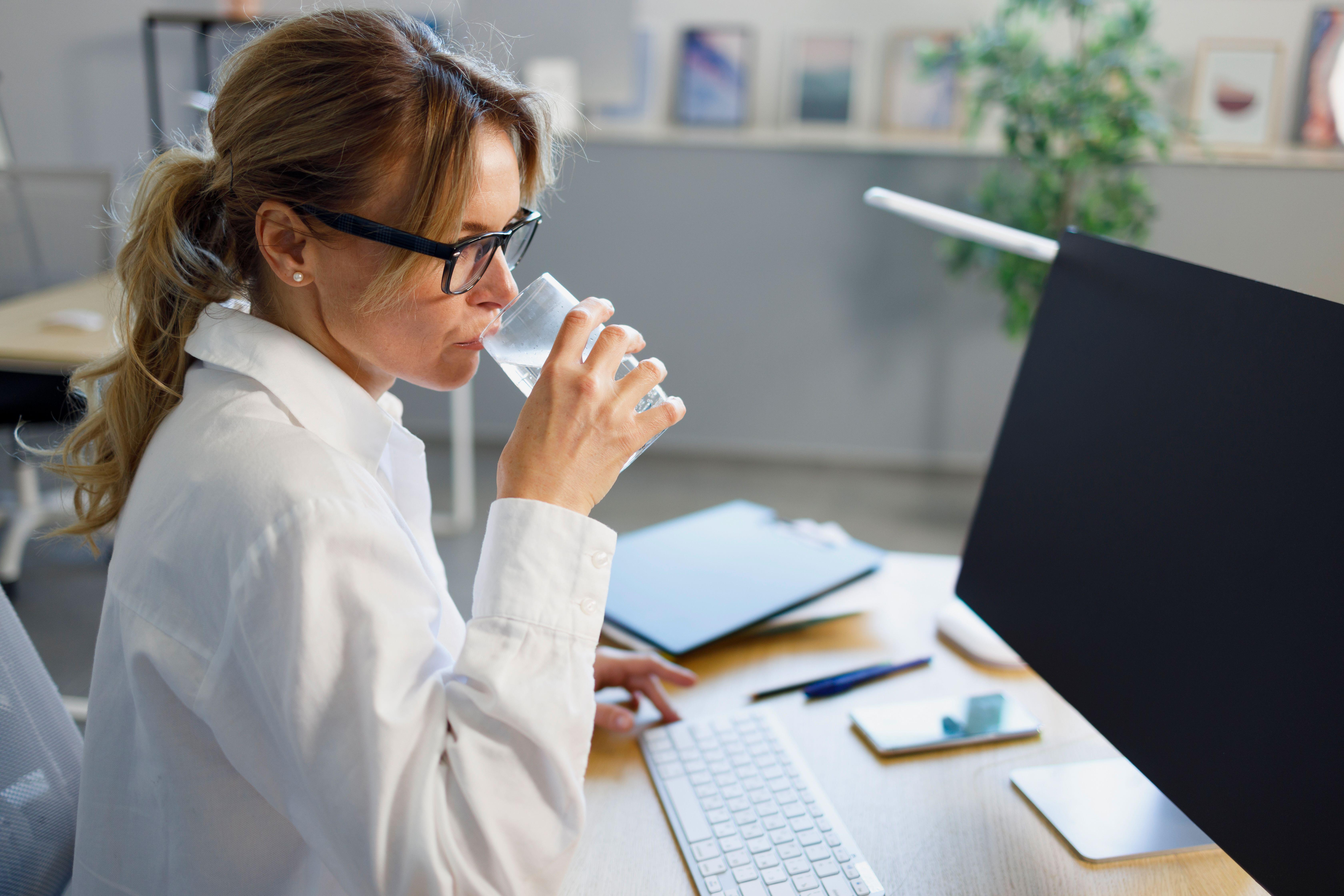 Side view of middle-aged woman drinking water sitting at a computer