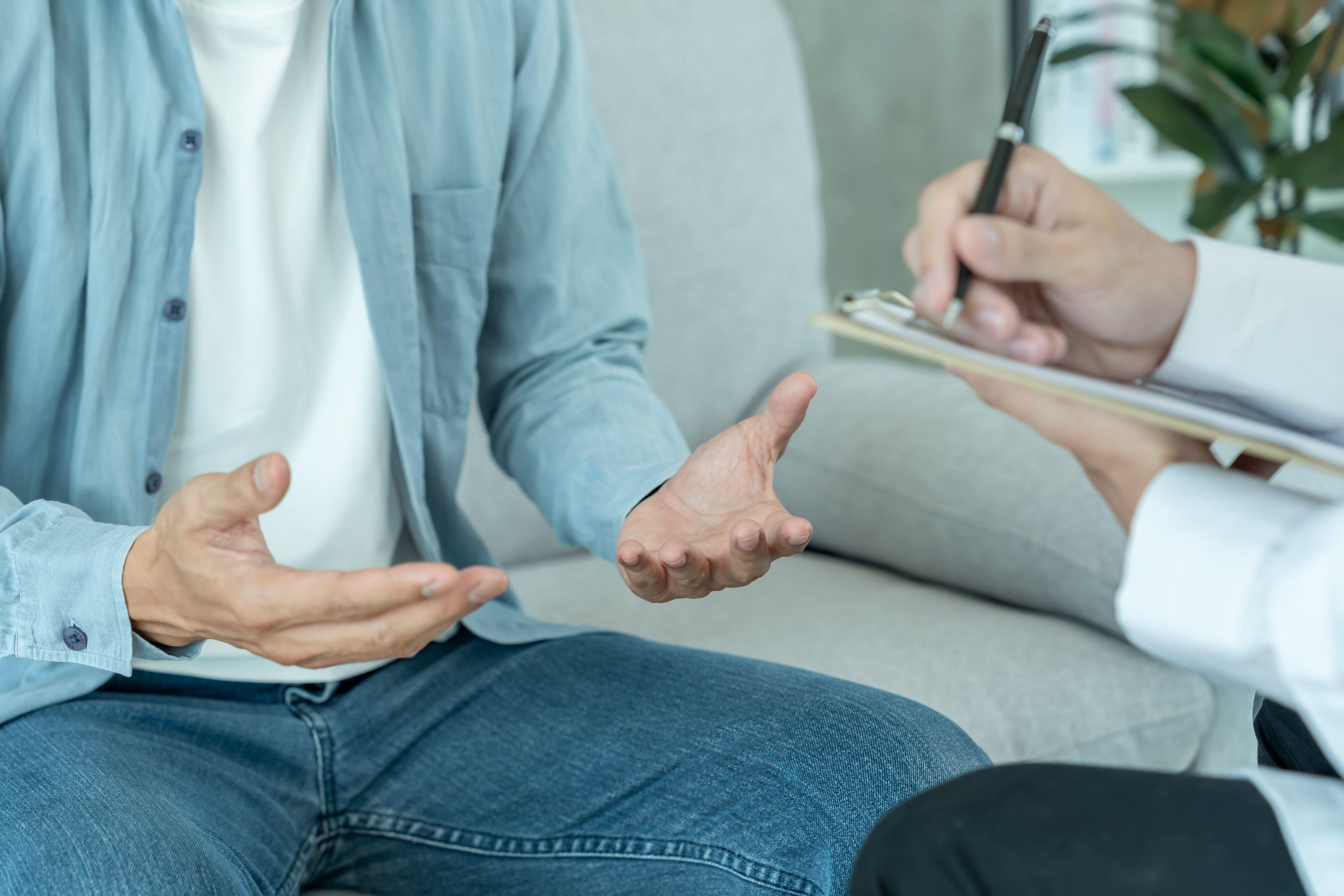 Cropped picture of man sitting on a sofa talking to a therapist 