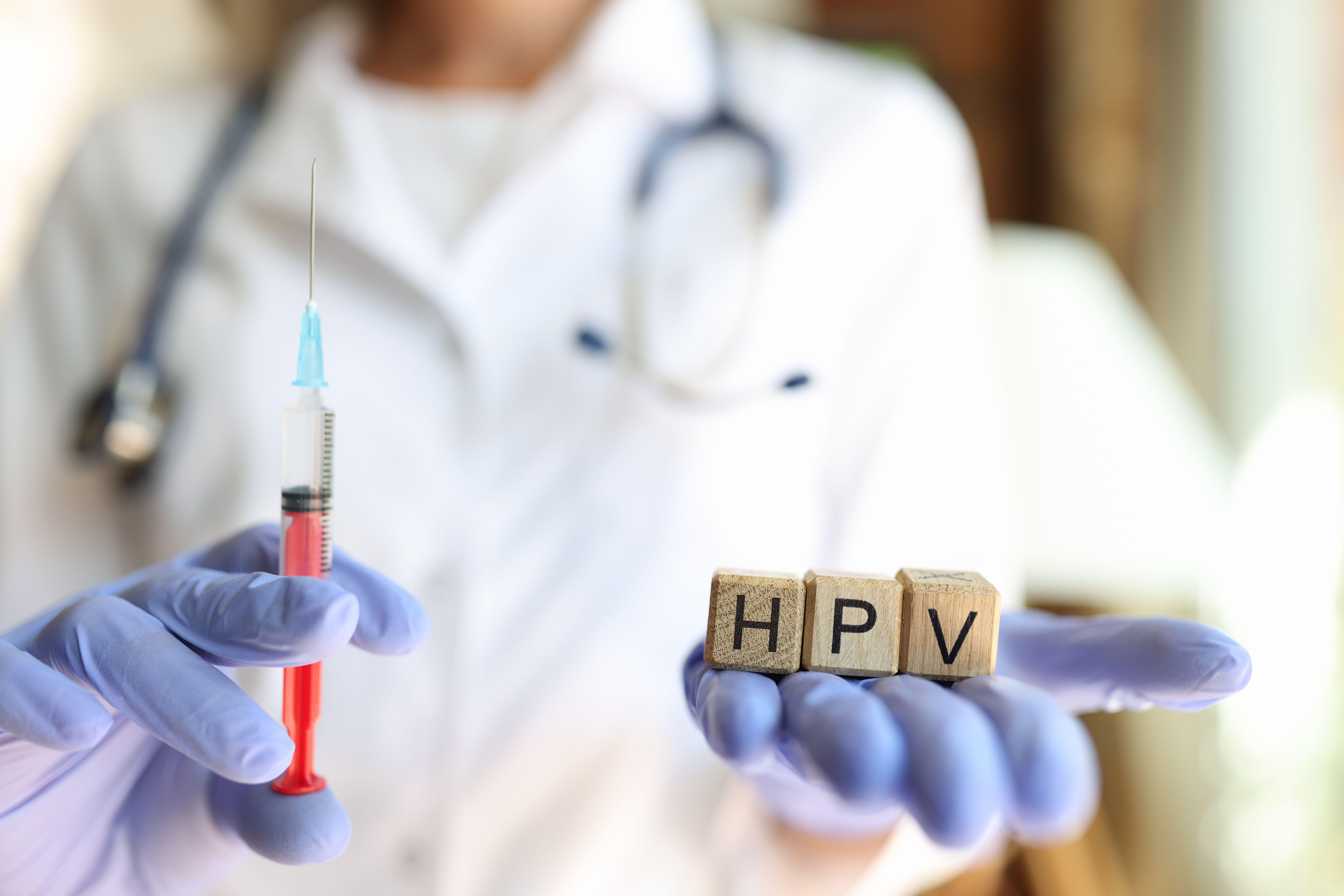 Doctor handing syringe and wooden blocks that spell out HPV 