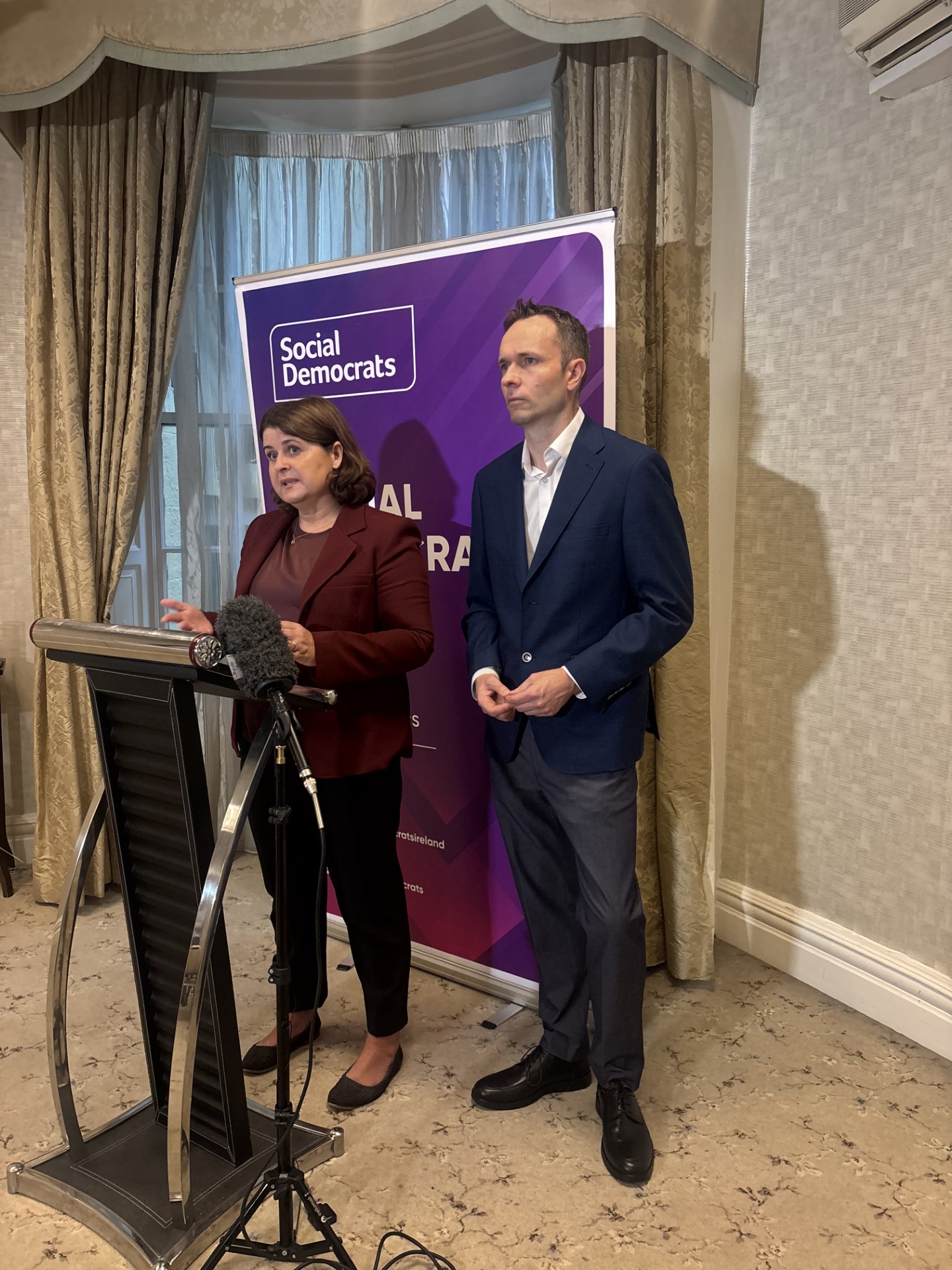 Jennifer Whitmore and Cian O'Callaghan standing next to each other while speaking from a lectern
