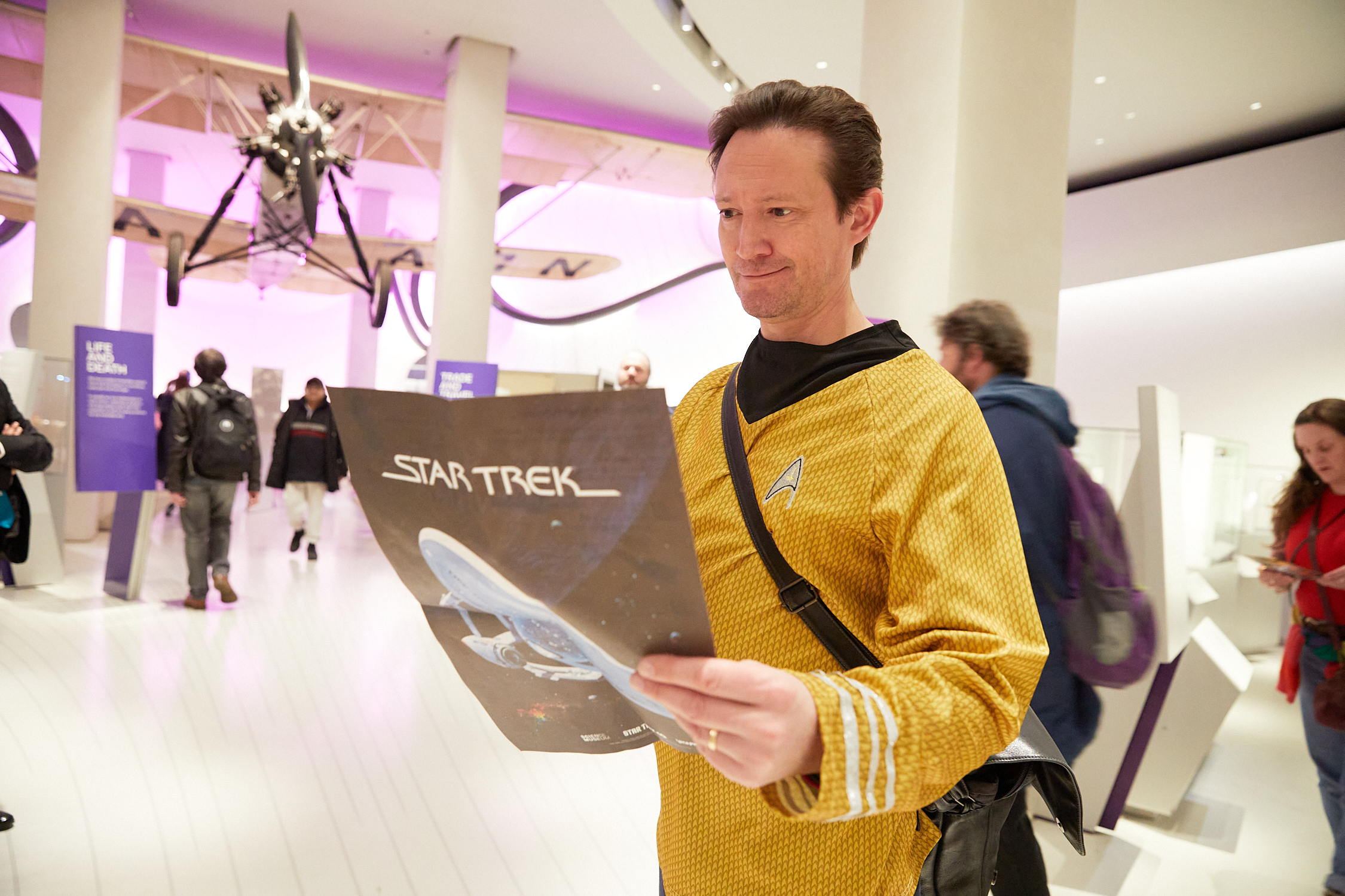 A man in a Star Trek uniform reading a Star Trek leaflet while standing in a museum