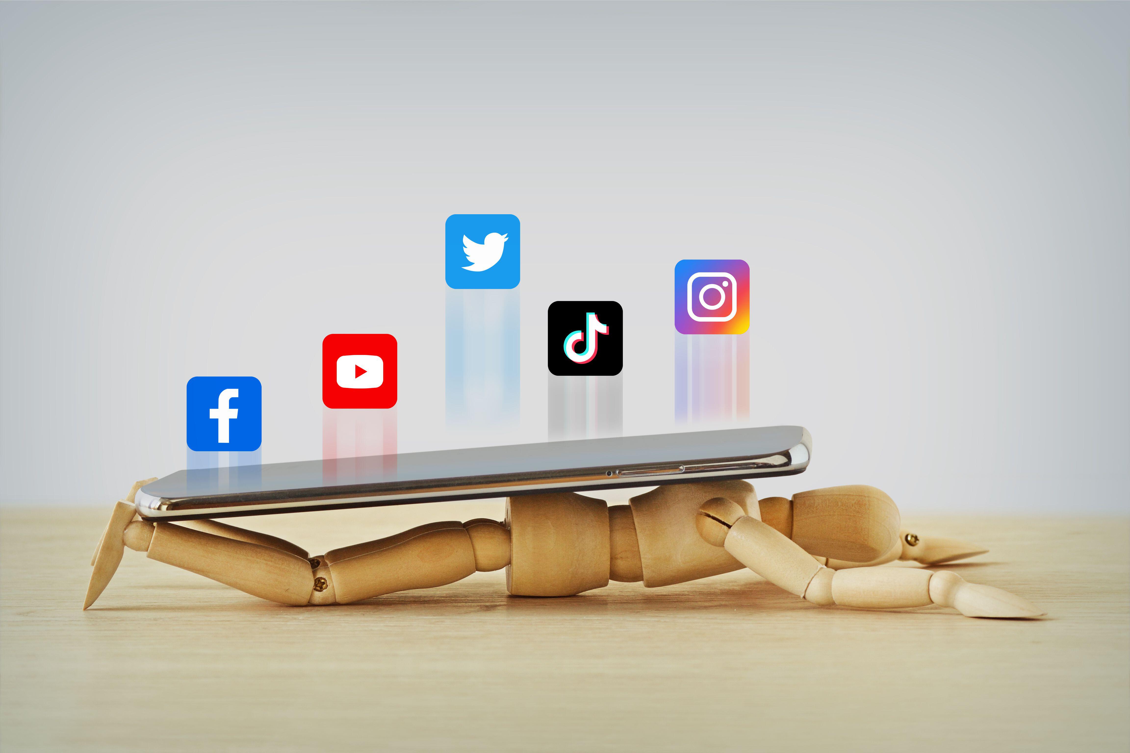 Wooden mannequin crushed under a smartphone with social media icons