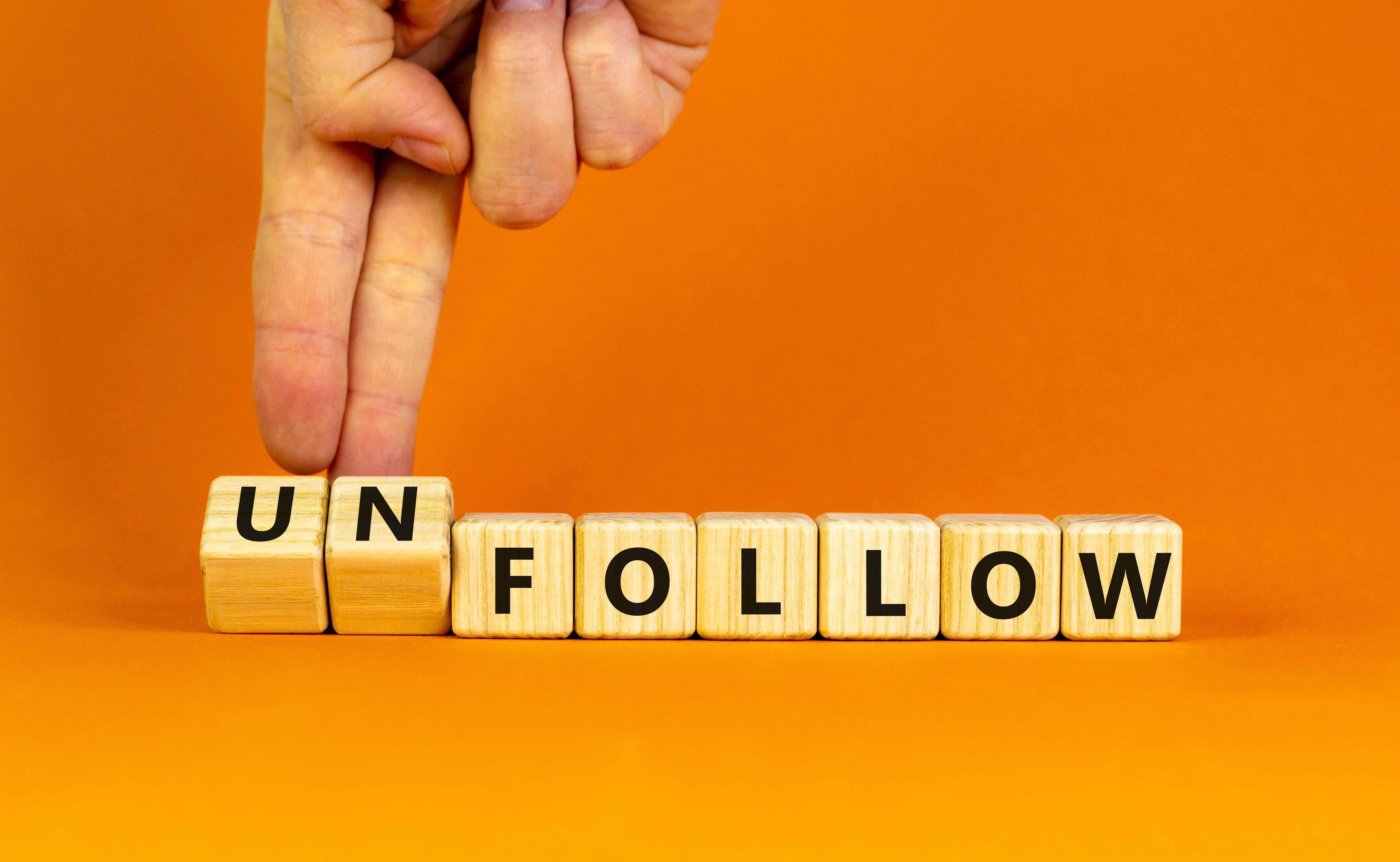 Hands turning over wooden blocks that spell out unfollow