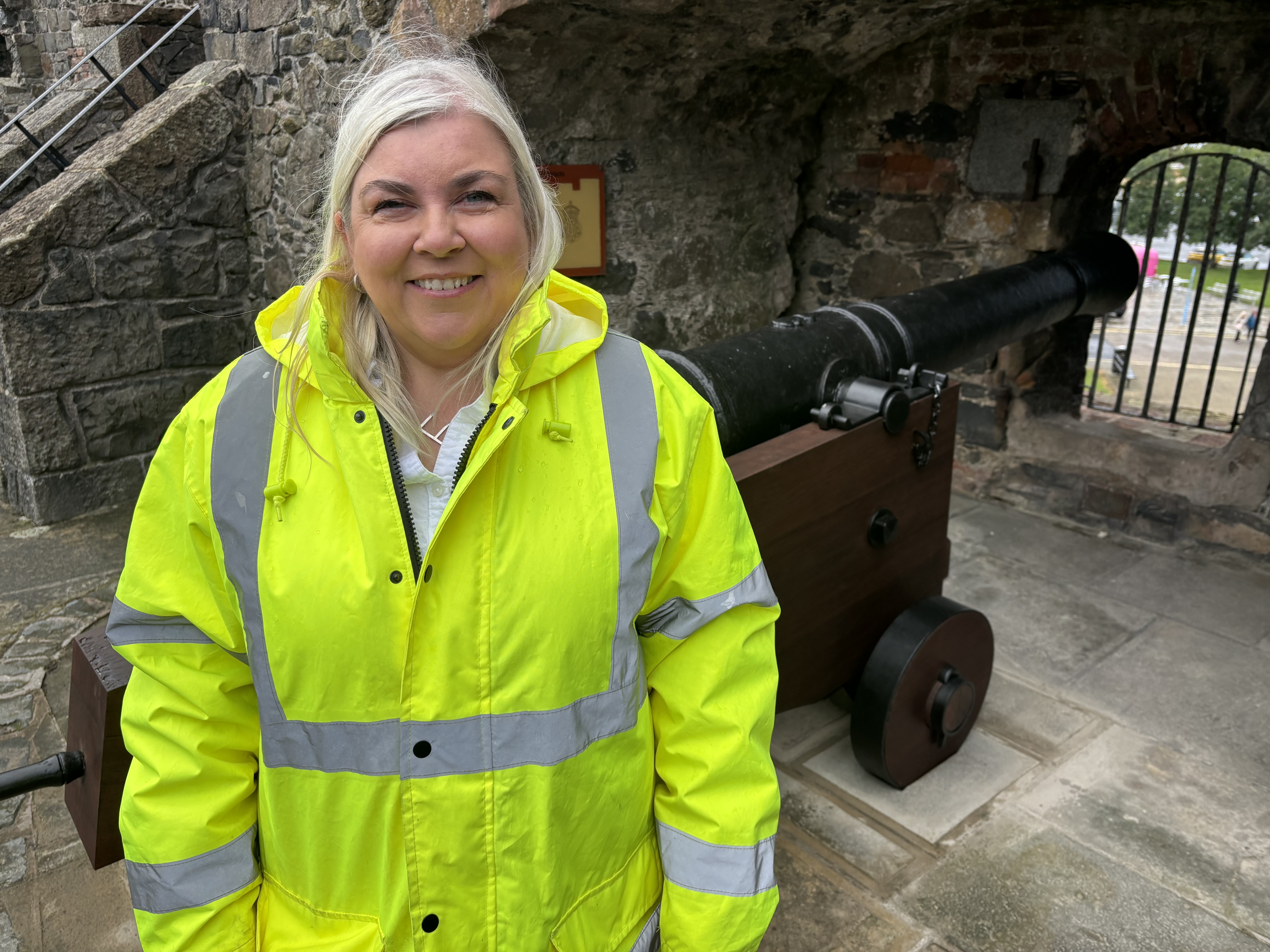 Edith Gowdy standing in front of a cannon smiling and wearing hi-vis