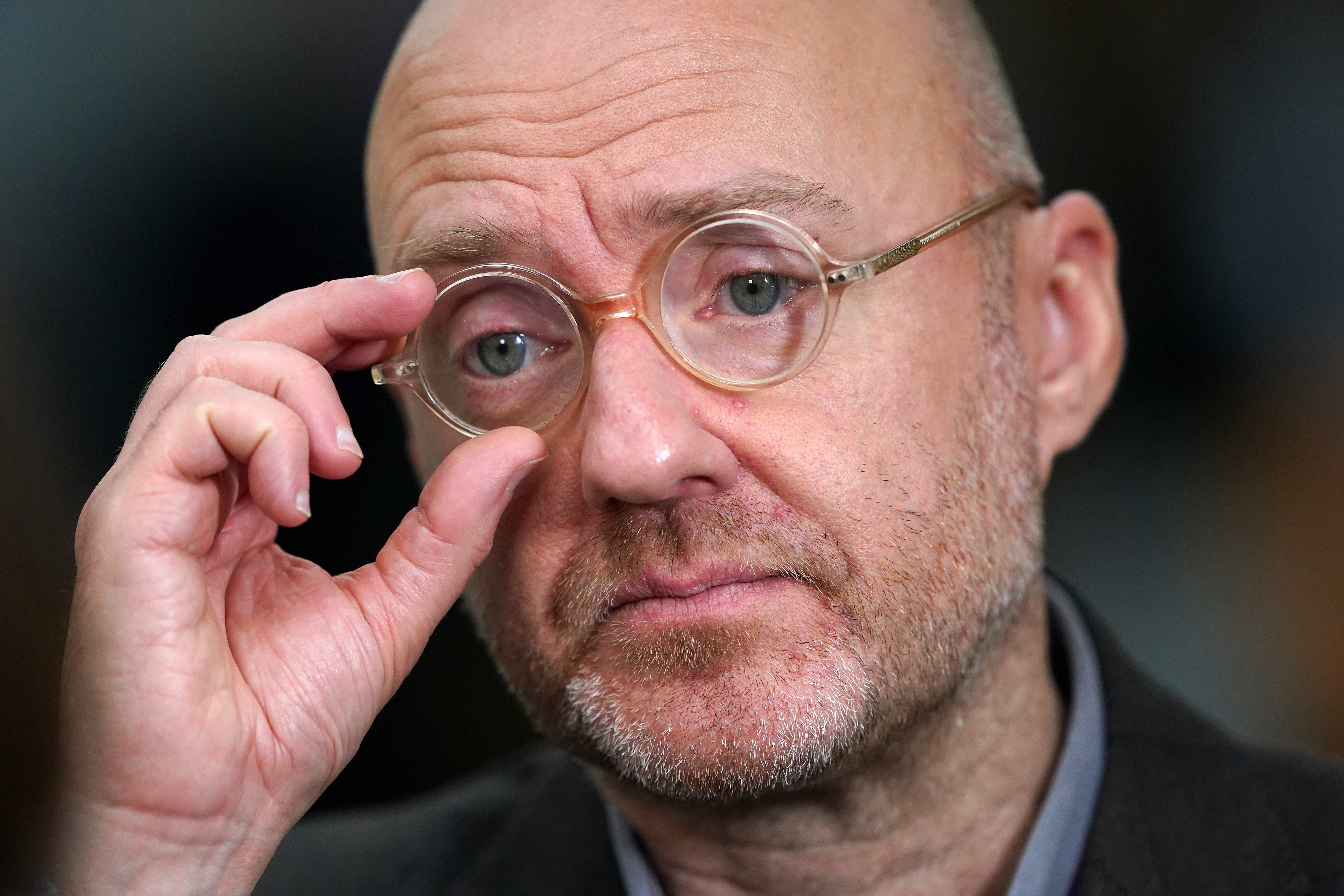 Headshot of Patrick Harvie, adjusting his round glasses