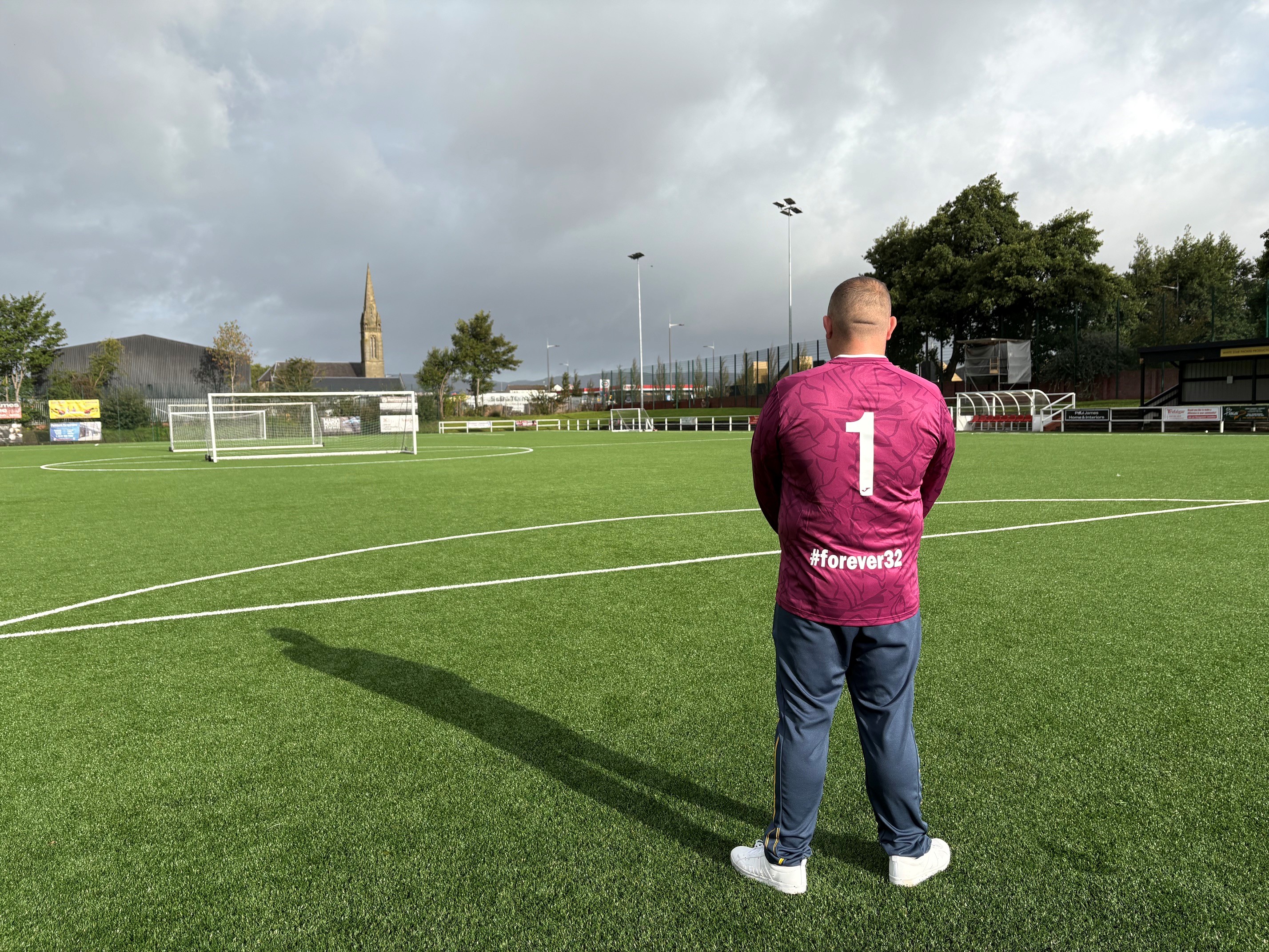 Back view of man in jersey reading 'Forever 32' next to football pitch