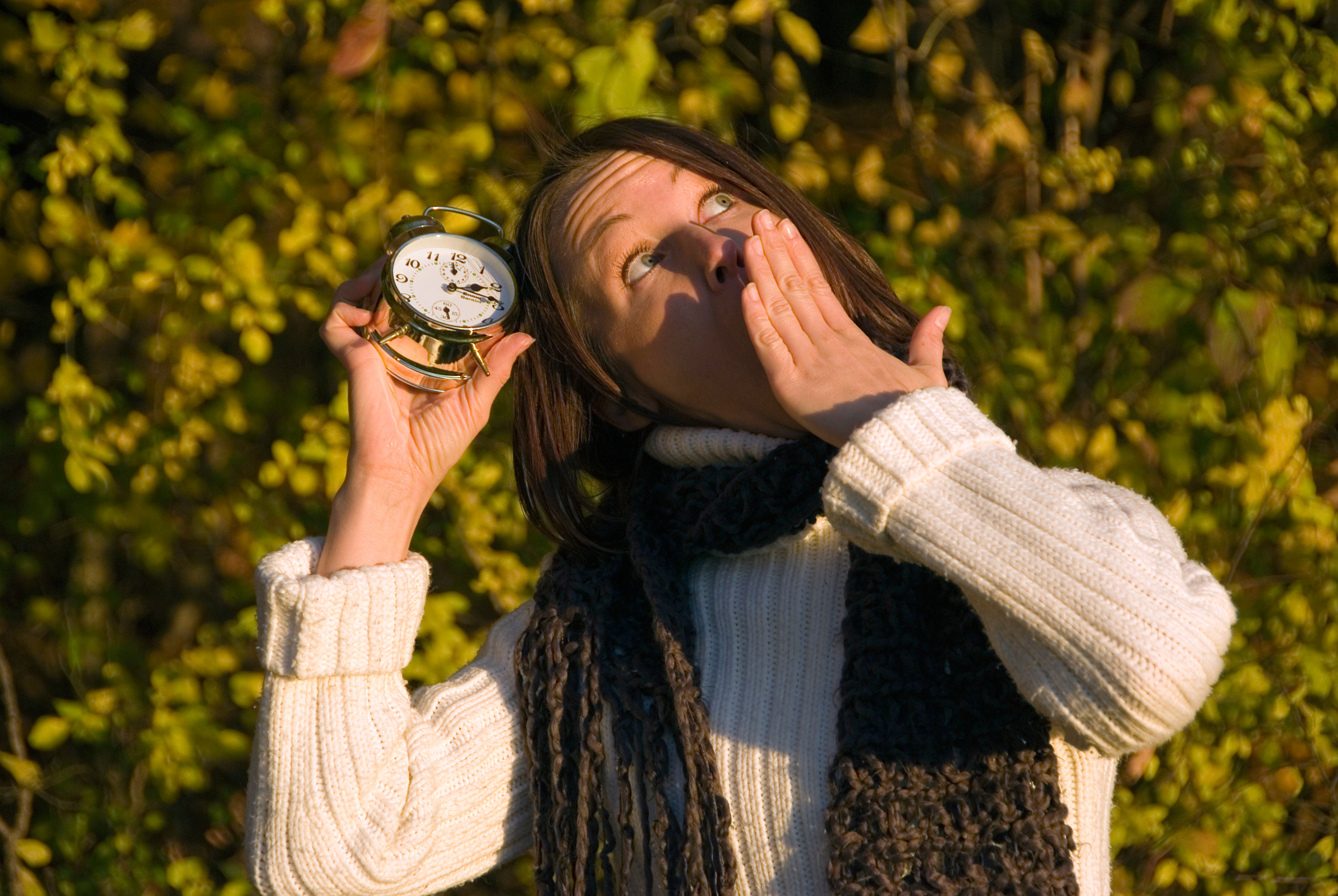 Woman yawning while holding a clock in her hand