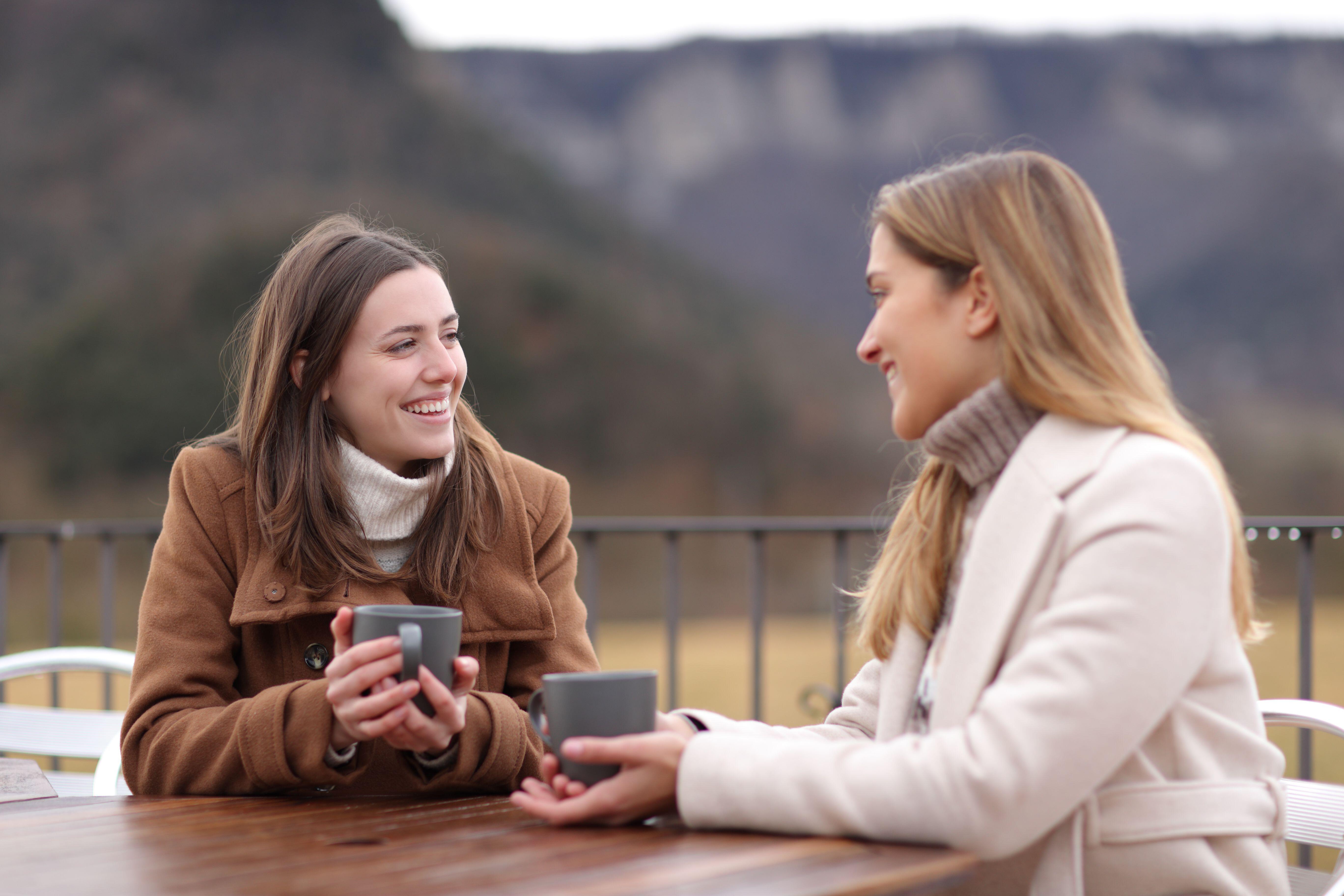 Two women drinking coffee and talking in winter sitting in a terrace