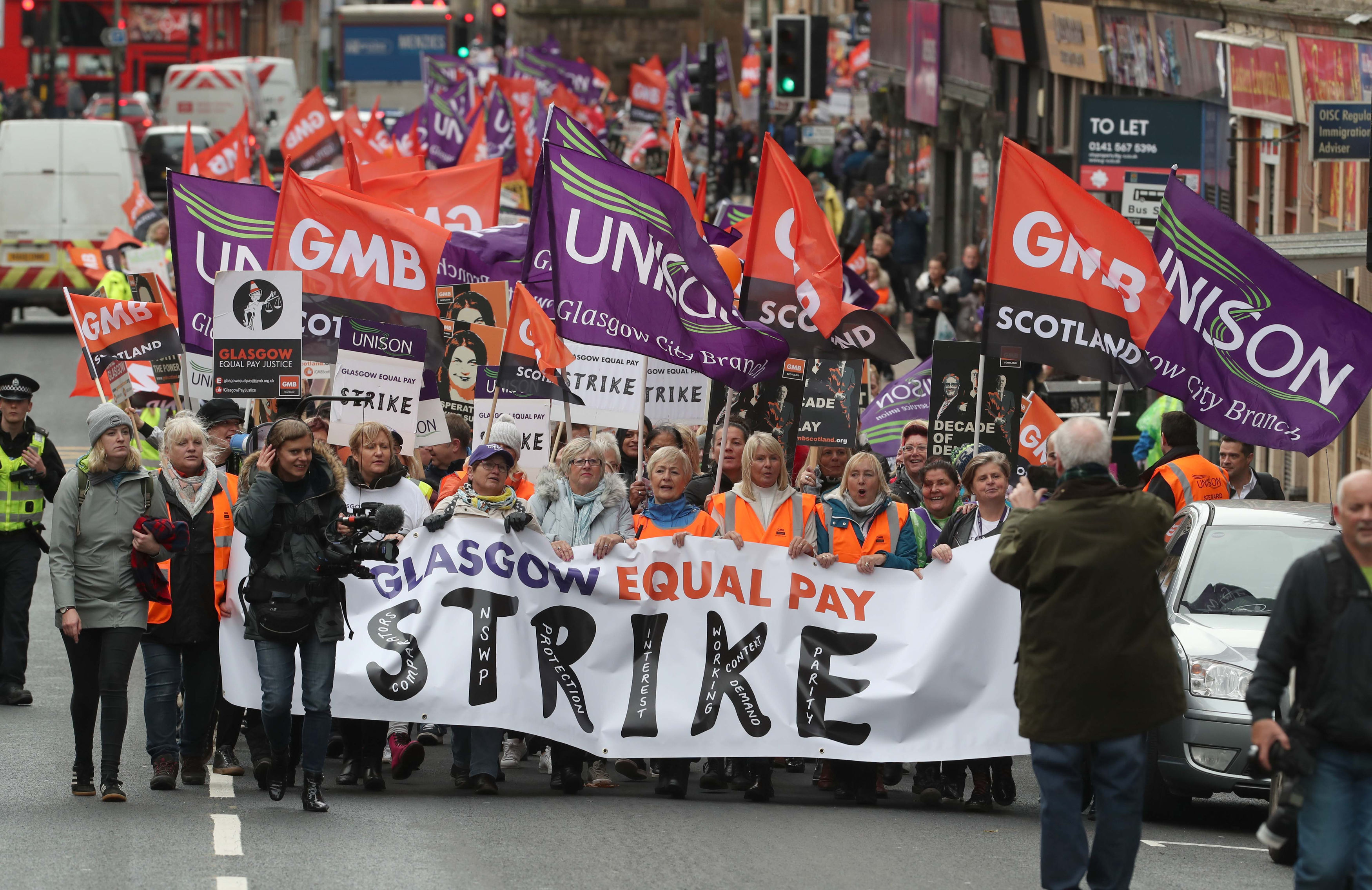 A large number of people taking part in a march, holding GMB and Unison flags and placards
