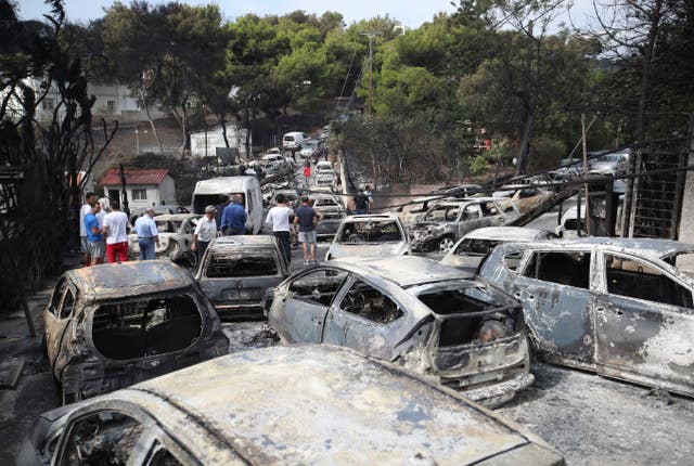 People stand amid the charred remains of burned-out cars in Mati east of Athens, Greece, in July 2018