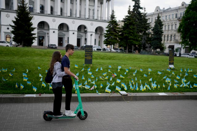 A couple ride a scooter in front of flags honouring soldiers killed fighting Russian troops in Independence Square in Kyiv, Ukraine