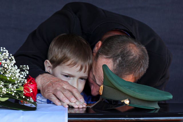 A boy and his grandfather mourn at a soldier's grave