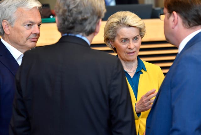 A blonde woman in a yellow jacket talks to three men gathered around her