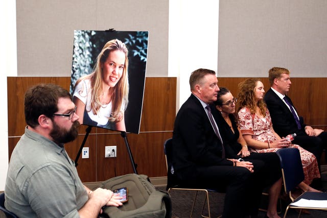 Chris Lambert, documentary podcaster, sits in front of a poster of Kristin Smart with family members nearby hours after a jury found Paul Flores guilty of the 1996 murder of Cal Poly student Kristin Smart 