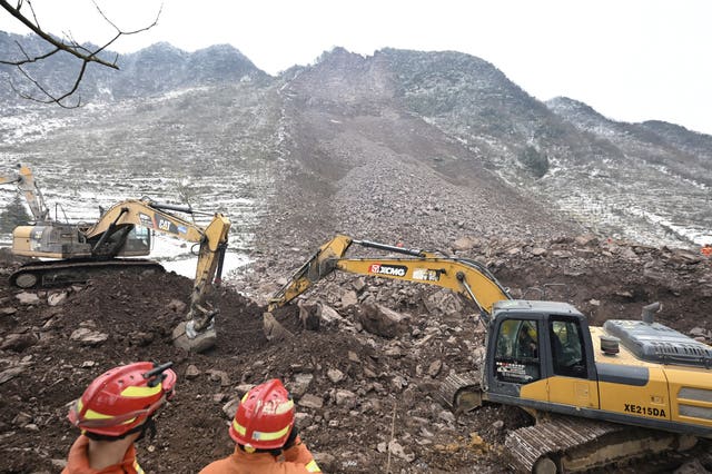 Rescue workers look on as excavators dig at the site of a landslide in Liangshui village 