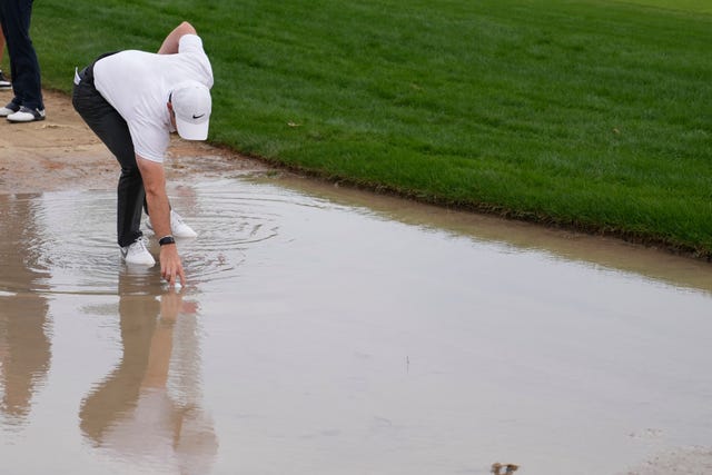Rory McIlroy retrieves his ball from standing water 