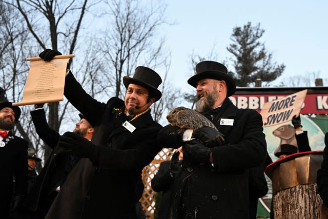 AJ Dereume holds Punxsutawney Phil while vice president Dan McGinley reads a scroll  