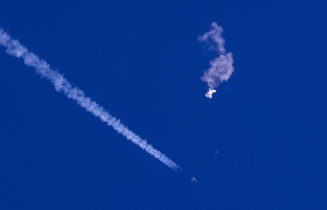 The remnants of a large balloon drift above the Atlantic Ocean, just off the coast of South Carolina, with a fighter jet and its contrail seen below it