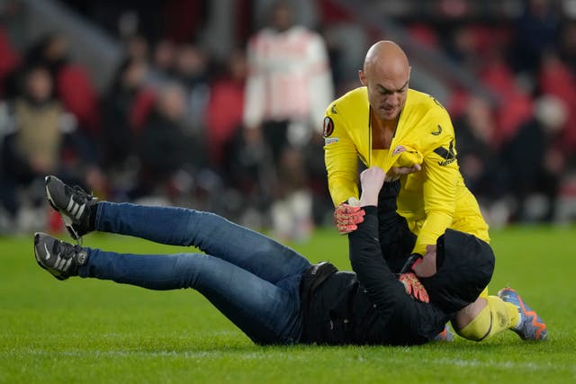 Sevilla’s goalkeeper Marko Dmitrovic restrains a PSV supporter 