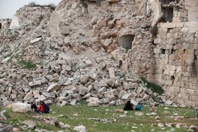 People sit by a building destroyed in recent earthquake in Aleppo, Syria