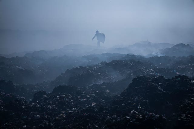 A Palestinian man collects plastic as smoke rises from a fire in a landfill, east of Gaza City