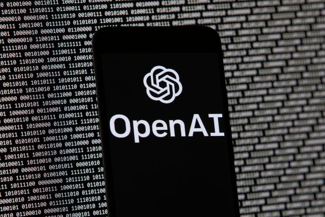 The OpenAI logo appears on a mobile phone in front of a computer screen with random binary data